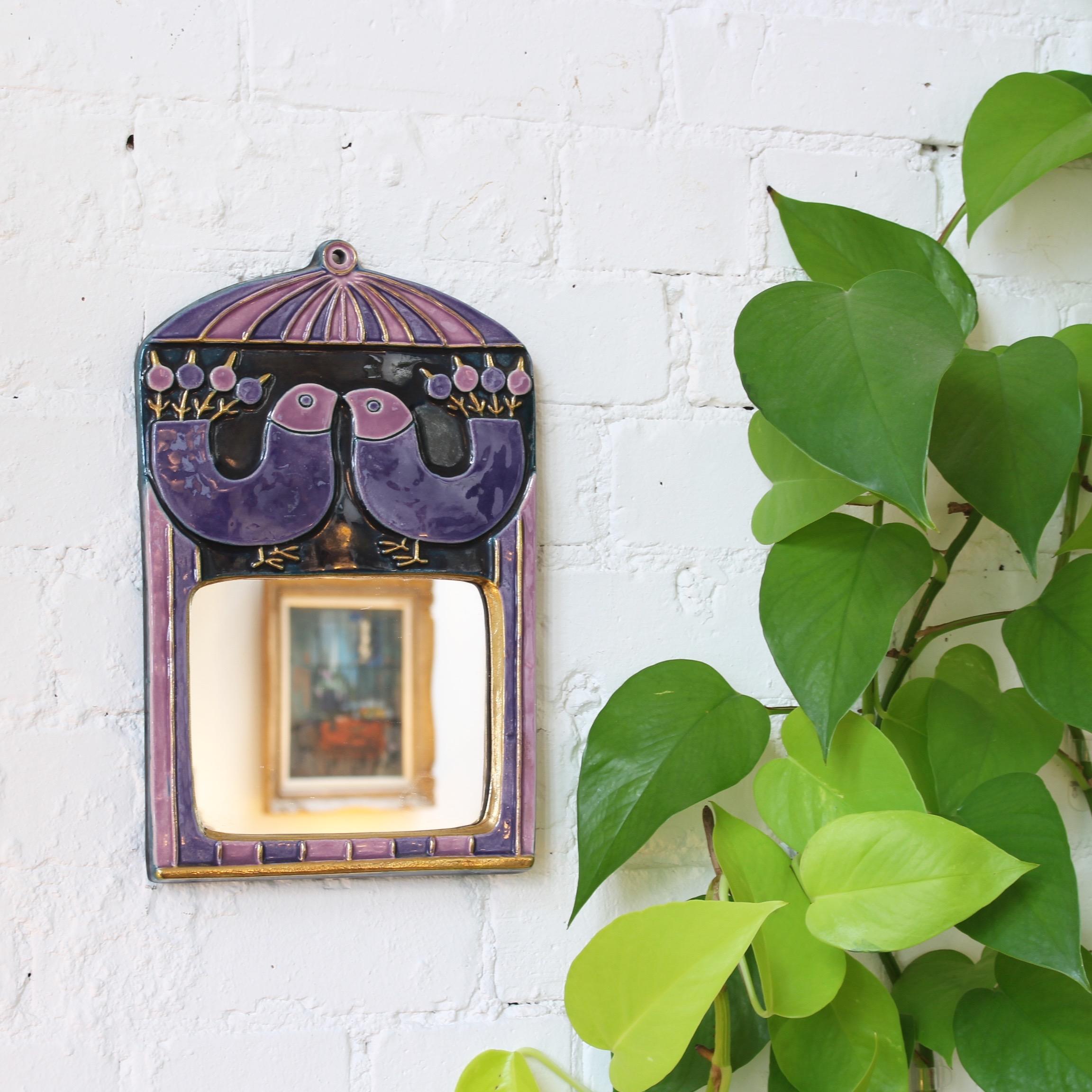 Ceramic wall mirror with purple and mauve glaze and stylized birds (circa 1970s) by Mithé Espelt. A delightful decorative wall mirror topped with a pair of whimsical birds above the curved rectangular mirror. The mirror is framed with a gold crackle