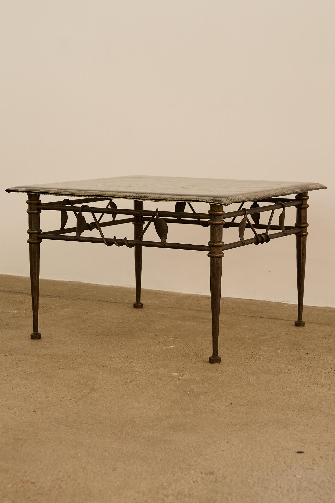 Cette table basse carrée des années 1970 présente un cadre en fer forgé à la main avec des détails de feuilles et de volutes, supportant un épais plateau en verre texturé. Les pieds fuselés élancés et la finition patinée soulignent l'approche