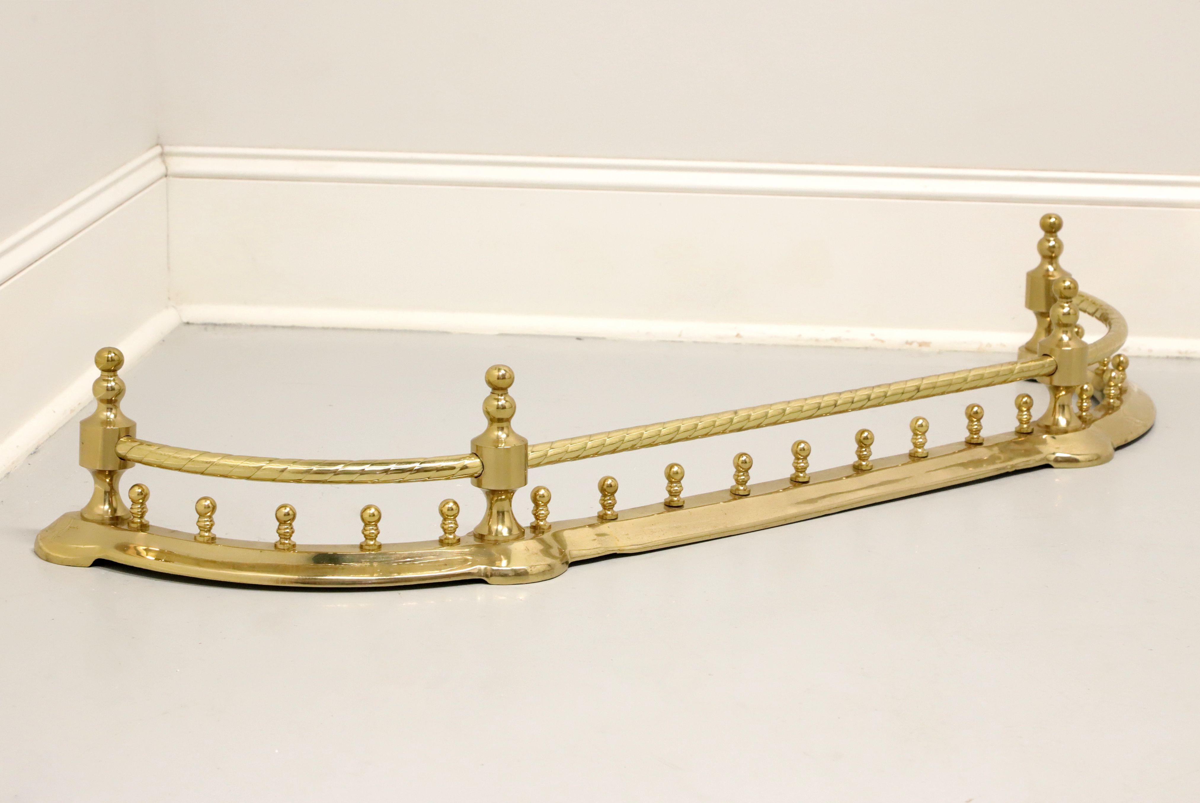 A Traditional style fireplace fender by Decorative Crafts. Solid hand crafted brass with a lacquered finish. Features an arched shape, swirl effect to top rail, four finial capped posts, and multiple decorative rounded posts to wider lower rail. No