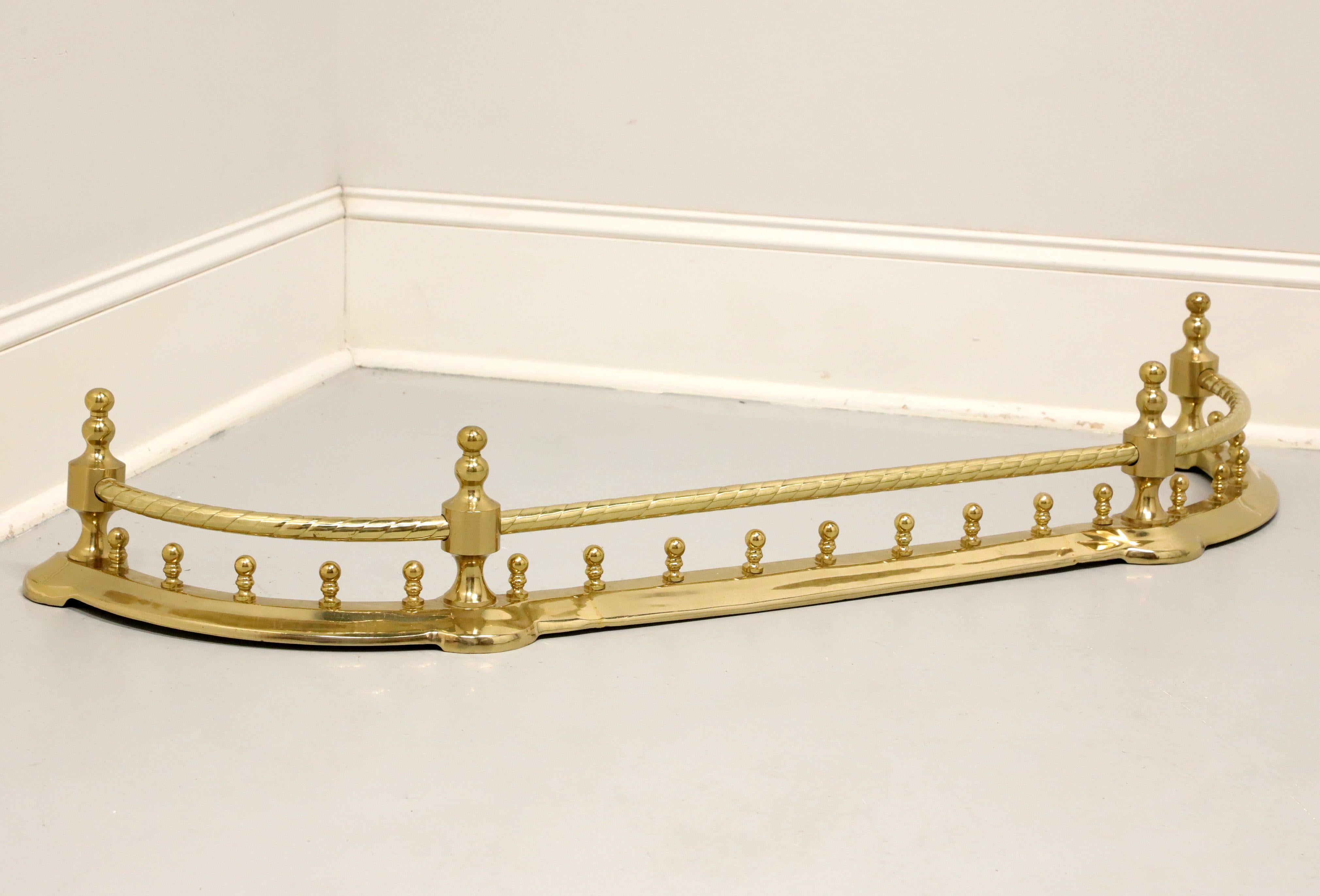 A Traditional style fireplace fender by Decorative Crafts. Solid handcrafted brass with a lacquered finish. Features an arched shape, swirl effect to top rail, four finial capped posts, and multiple decorative rounded posts to wider lower rail. No