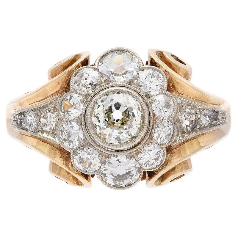 A highly decorative diamond retro ring, ca. 1950s. The ring is in 14k yellow gold and has a very fine craftsmanship. The profile has a swirly curvaceous design while the top of the ring is set with a diamond entourage around the centre stone. The