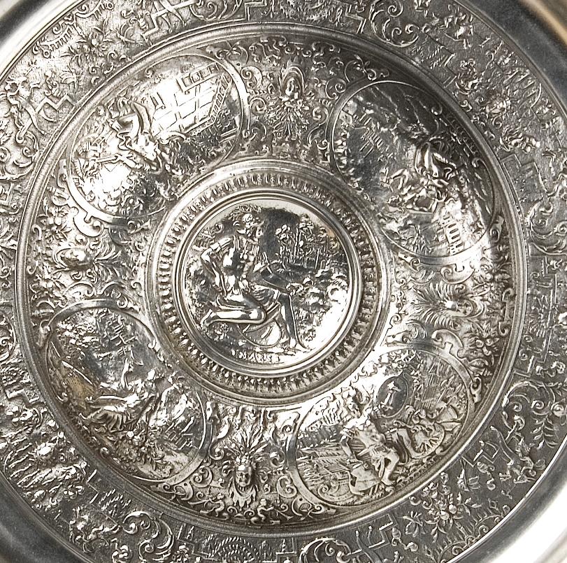Pewter decorative plate decorated with a series of stripes with figurative scenes and architectural and vegetable elements of clear classicist inspiration and Renaissance memory. In the center is a male figure that recalls in his posture the Ares