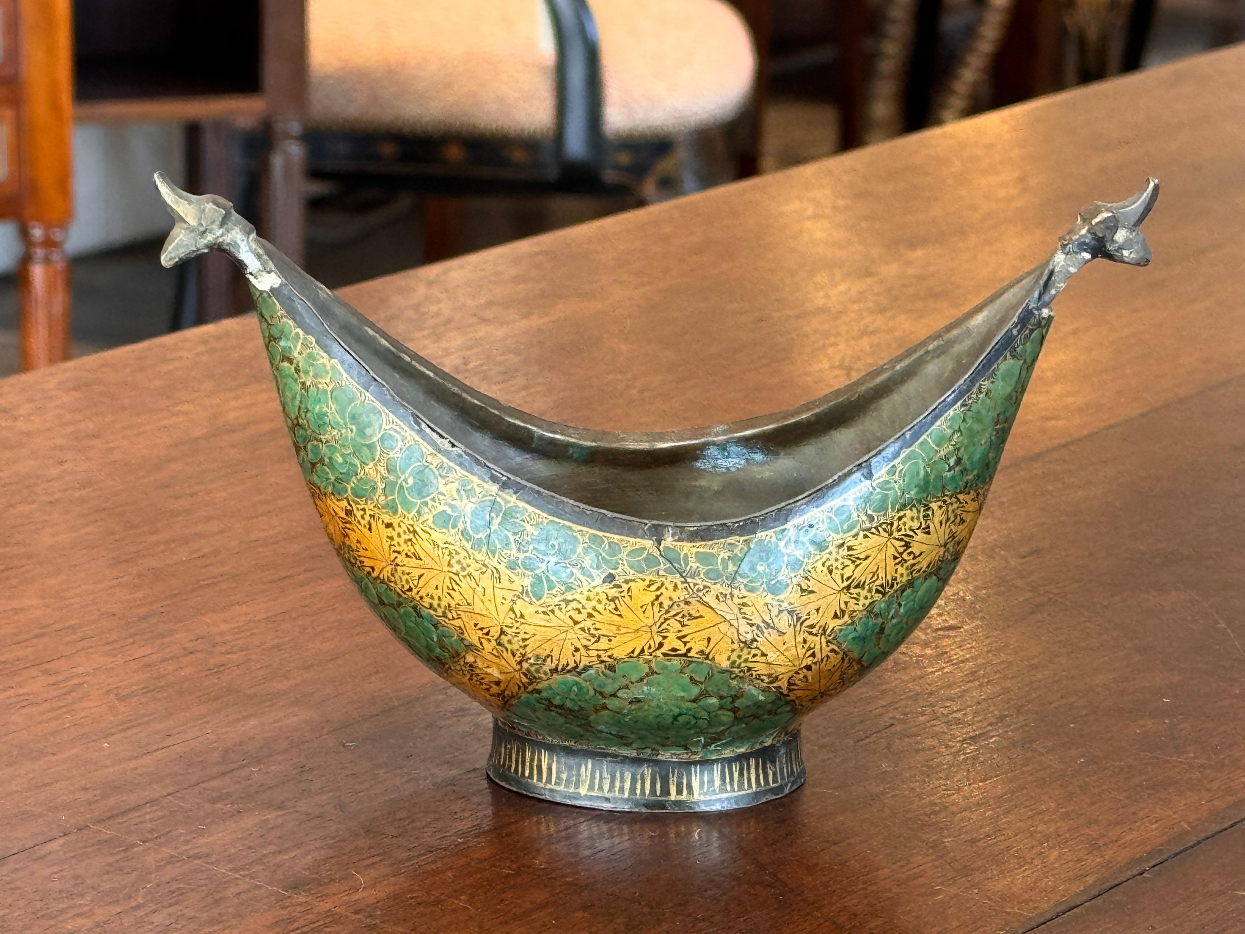 Enameled metal bowl with gently curved sides and stylized animal-form terminals. Hand-enameled floral and geometric motifs cover the interior and rim; the close-up shows fine brushwork and layered enameling. Clean proportions, solid metal