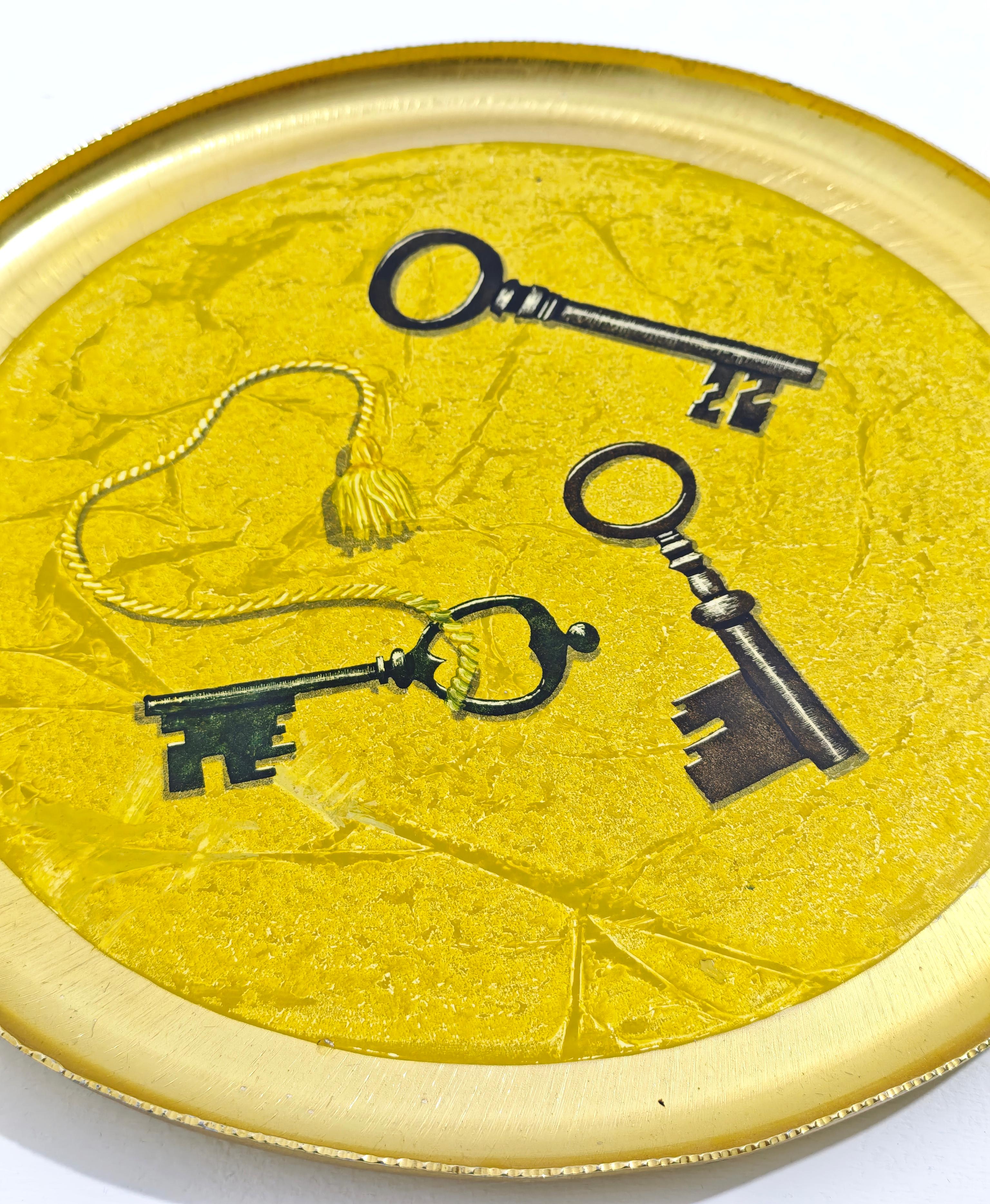 Bandeja decorativa redonda, de acero con acabado dorado. La bandeja tiene un diseño vintage. Está decorado con tres ilustraciones de llaves esqueleto.
Una de las llaves tiene una pequeña borla sujeta como elemento decorativo adicional. El borde está