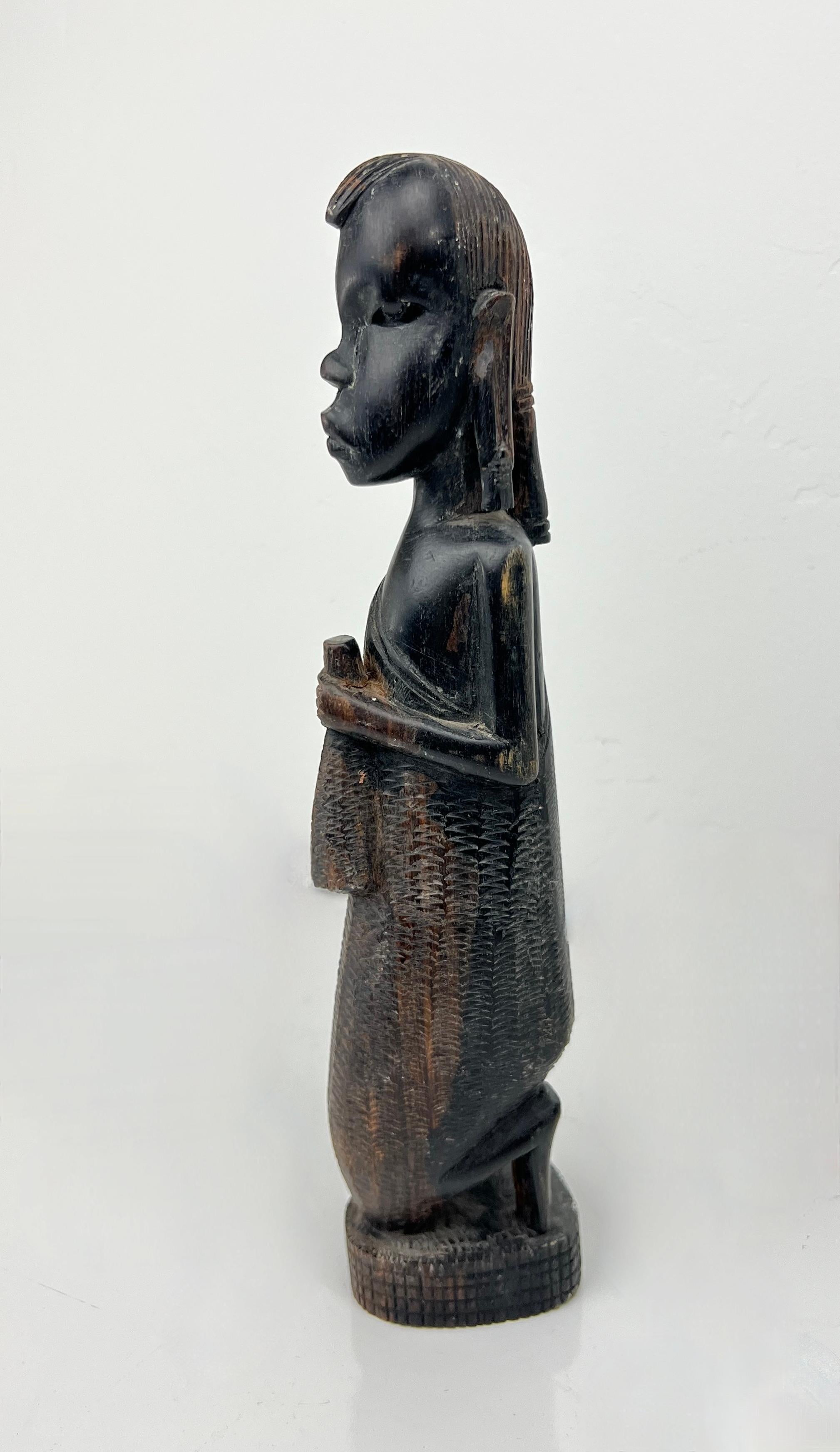 Hand-Carved African Sculpture of Kneeling Male made of Dark Wood.  Hand-carved in Kenya. This carving is gorgeously detailed with a smooth sculpted face, hair tied back and ears adorned with long earrings.  The tribal male appears to be holding a