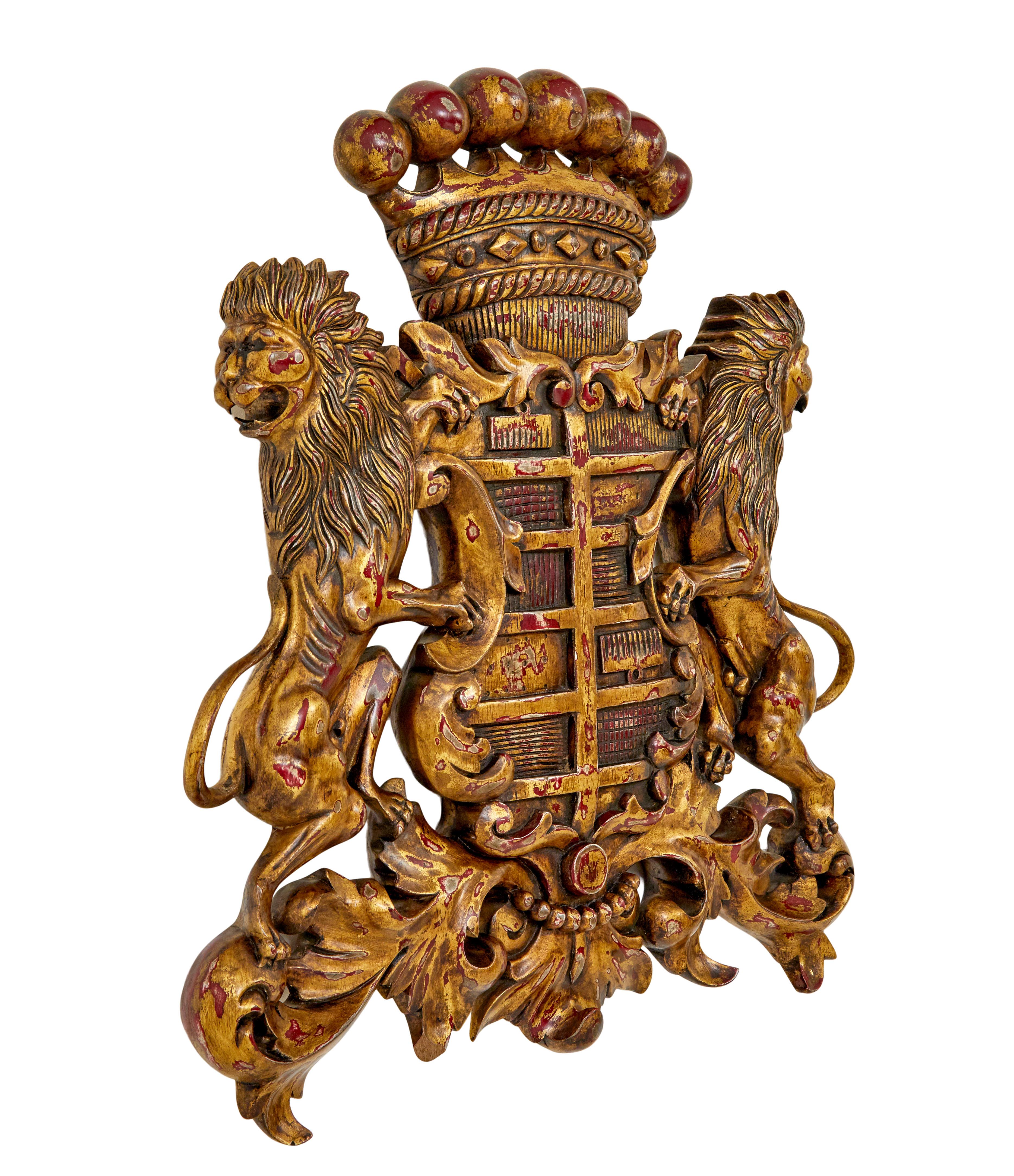 Good quality gilt colored coat of arms. Central shield with acanthus decoration, flanked either side by outward facing standing lions.

Gilt has been worn through to allow the red base to show and create contrast.

Strung at the back and ready to
