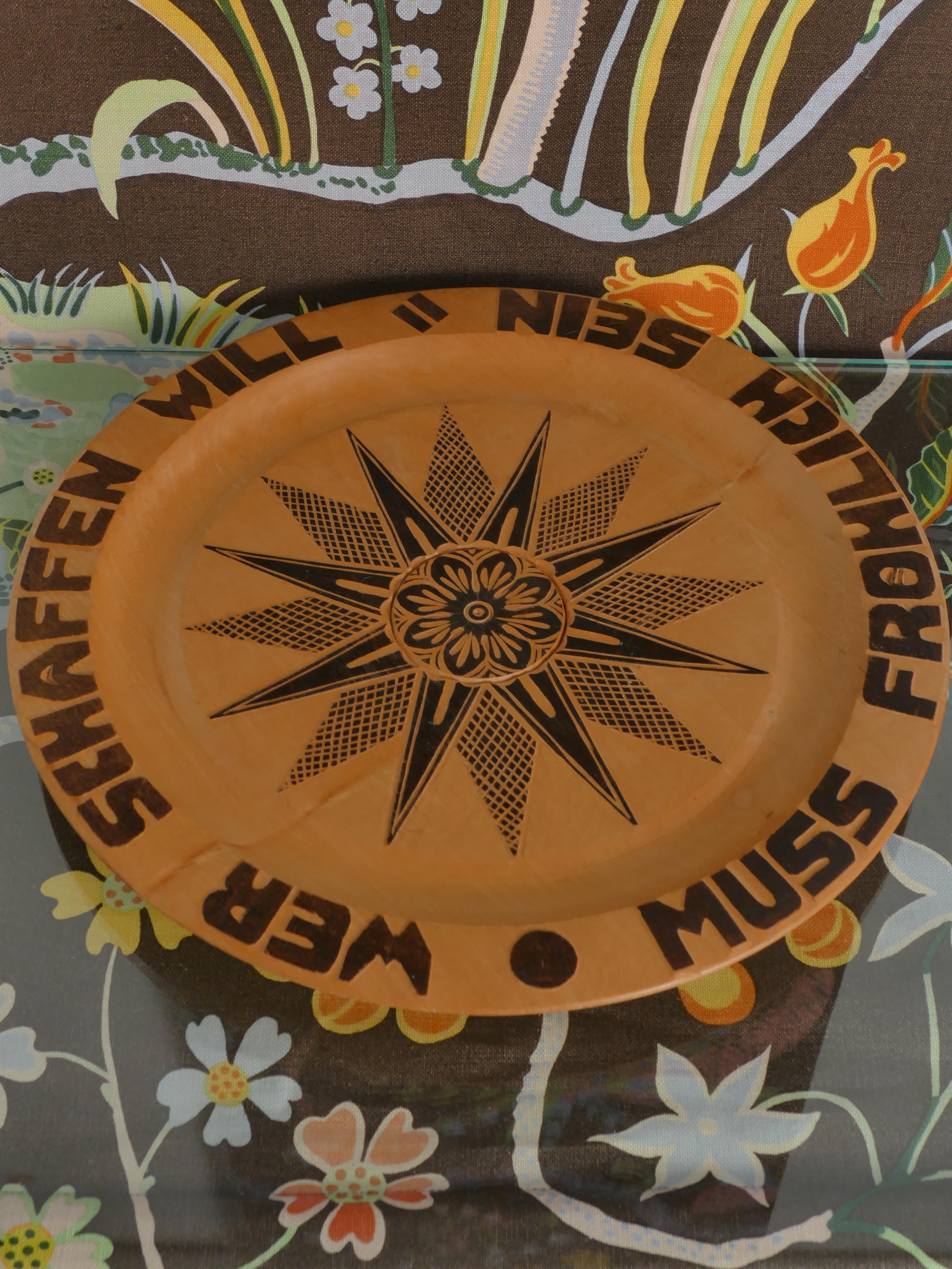 Dieser stilvolle, handgeschnitzte Holzteller im Volkskunststil weist komplizierte pyrografische Elemente auf - eine traditionelle Holzbrenntechnik, mit der dekorative Muster erzeugt werden. Das Design dreht sich um zwei sich überlappende 8-zackige