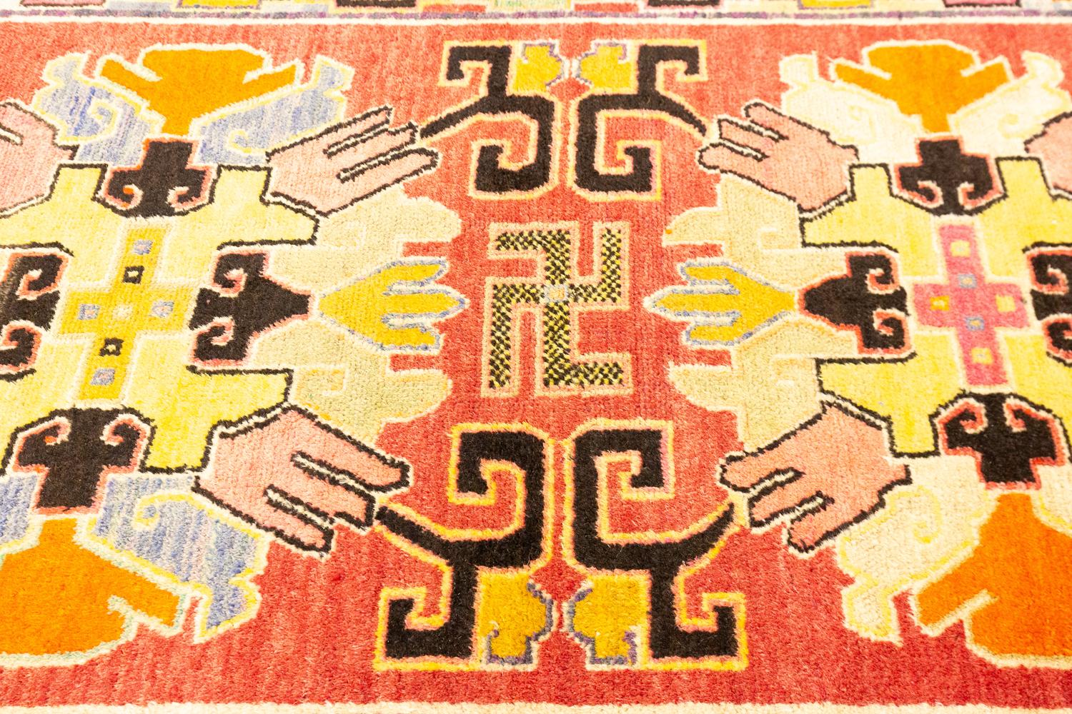 This is an antique Tibetan rug woven during the first quarter of the 20th century circa 1920 and measures 150 X 85CM in size. Its design consists of two geometric medallions with a center swastika motif that separates them set on a light red