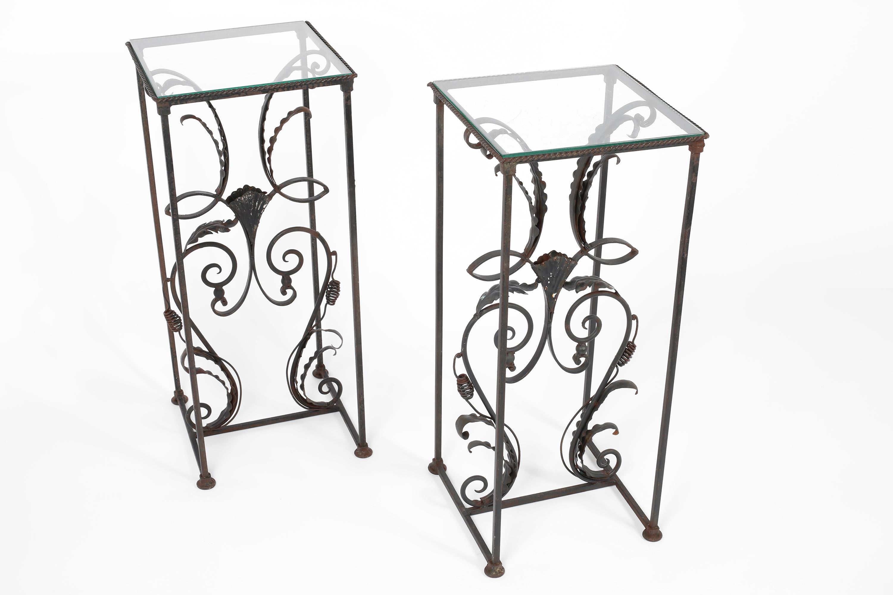 A pair of anthracite grey painted ironwork plinths or side tables with square glass tops. The highly decorative frames feature stylised acanthus leaves, vine tendrils and shells with a twisted rope trim to the tops. French, mid to late 20th century.