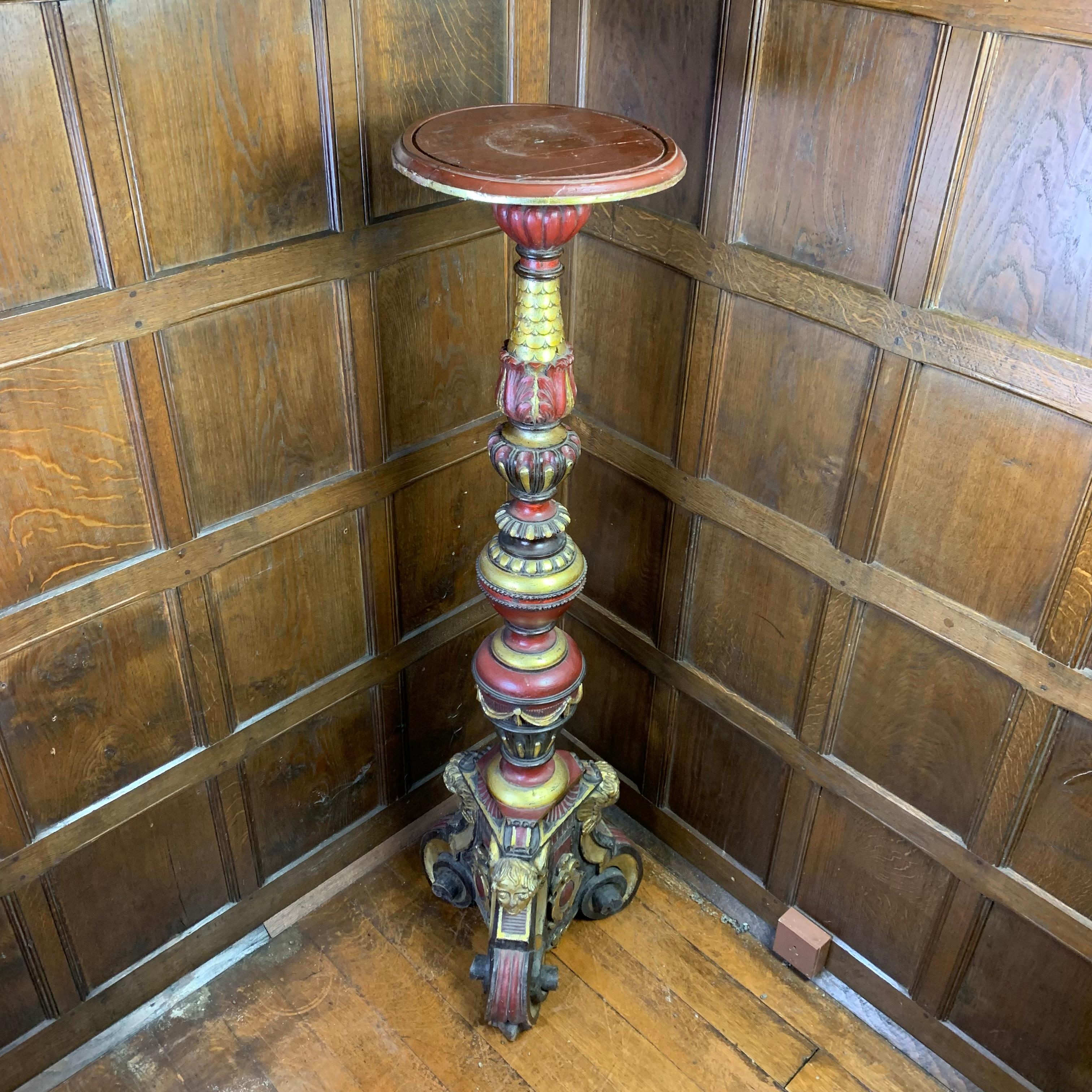 A highly decorative painted and gilded display pedestal with a circular stand at the top, above a profusely carved column and standing on a triform base with figural heads and scrolled feet. Painted trroughout in black and red with abundant gilded