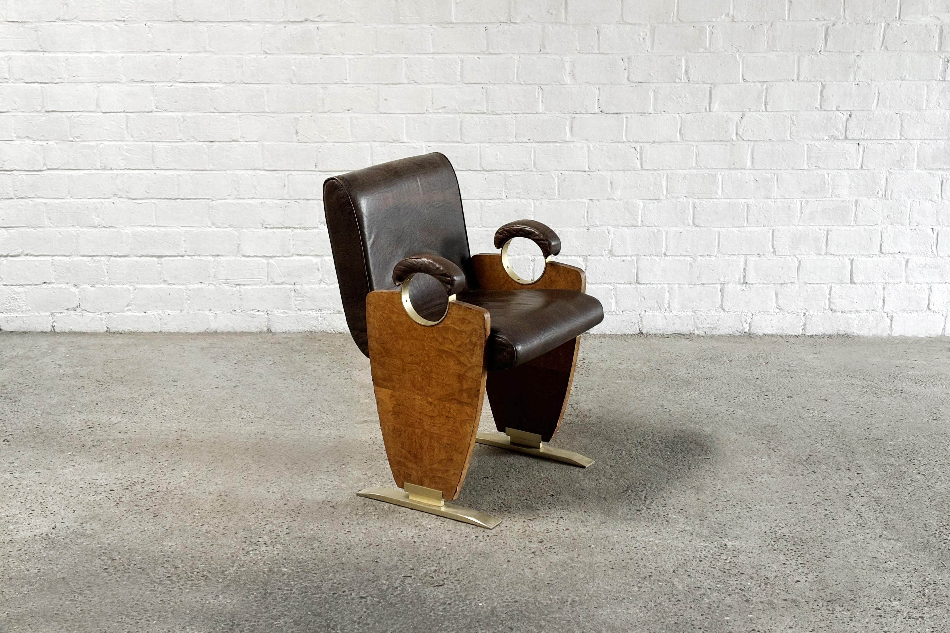 A peculiar wooden lounge or side chair with skai leather upholstery in Art Deco style, 2nd half of the 20th century. The two round armrests and legs are covered with brass-colored metal accents. The wood is veneered with burl walnut wood. This is a
