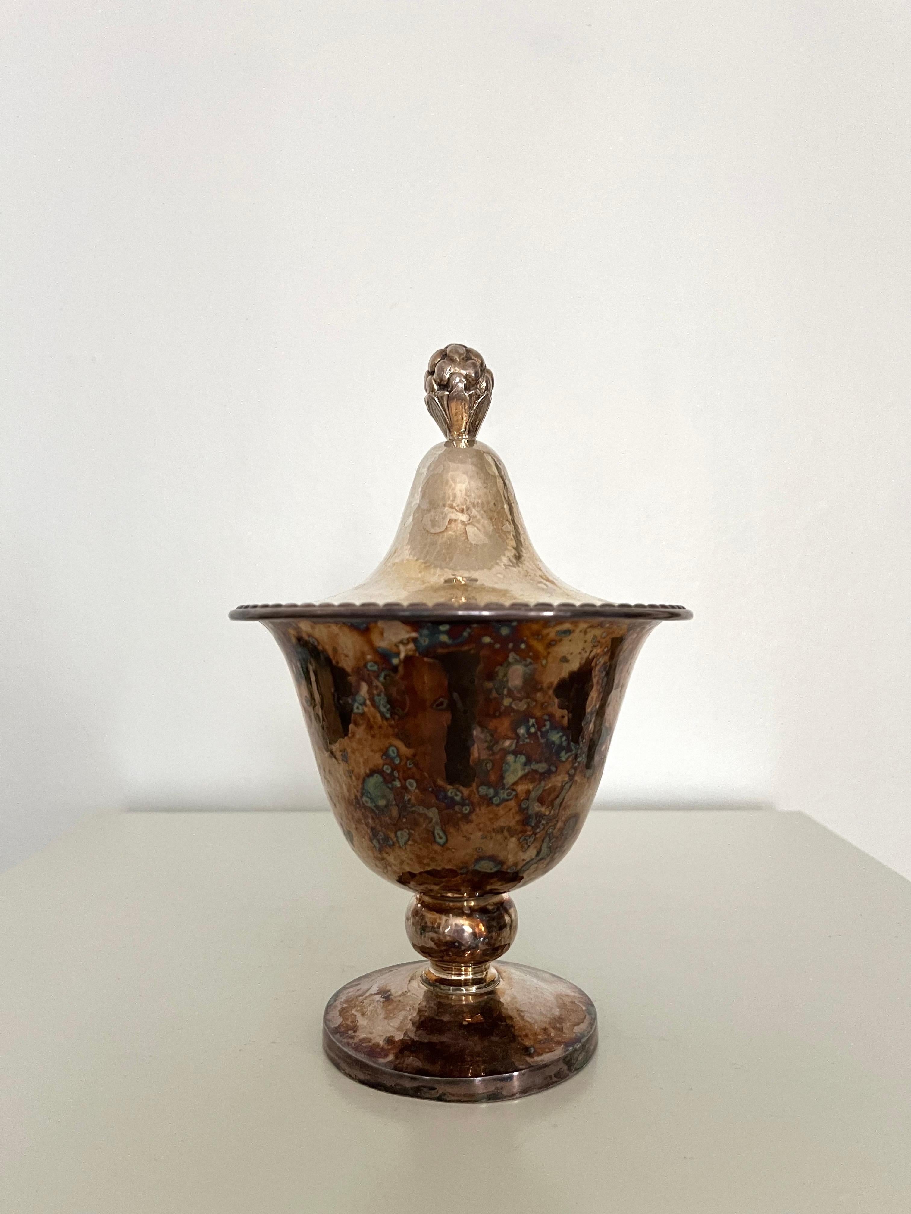Dekorative Zucker-/Marmeladendose aus Metall mit Deckel und Tannenzapfen, ca. 1920-30er Jahre

Elegante Schale mit Deckel aus Metall (nicht gestempelt; möglicherweise versilbert), in subtiler Pokalform auf rundem Fuß. Der sanft ausgestellte Korpus