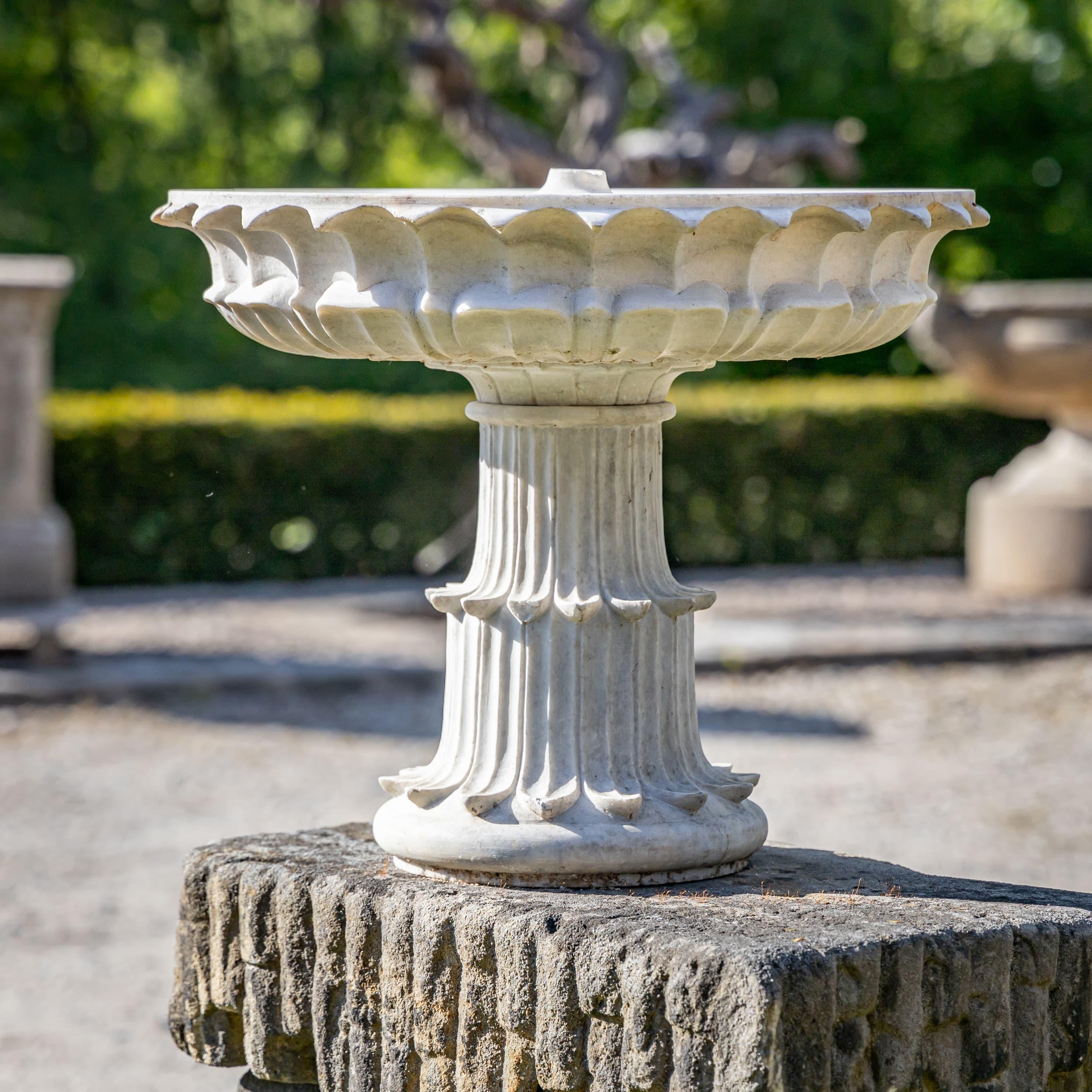 Decorative bowl made of white marble with a chalice-shaped pedestal and finely detailed leaf ornamentation. The clean contouring and precise execution of the surrounding leaf motifs give the piece its classical appearance and artisanal refinement.