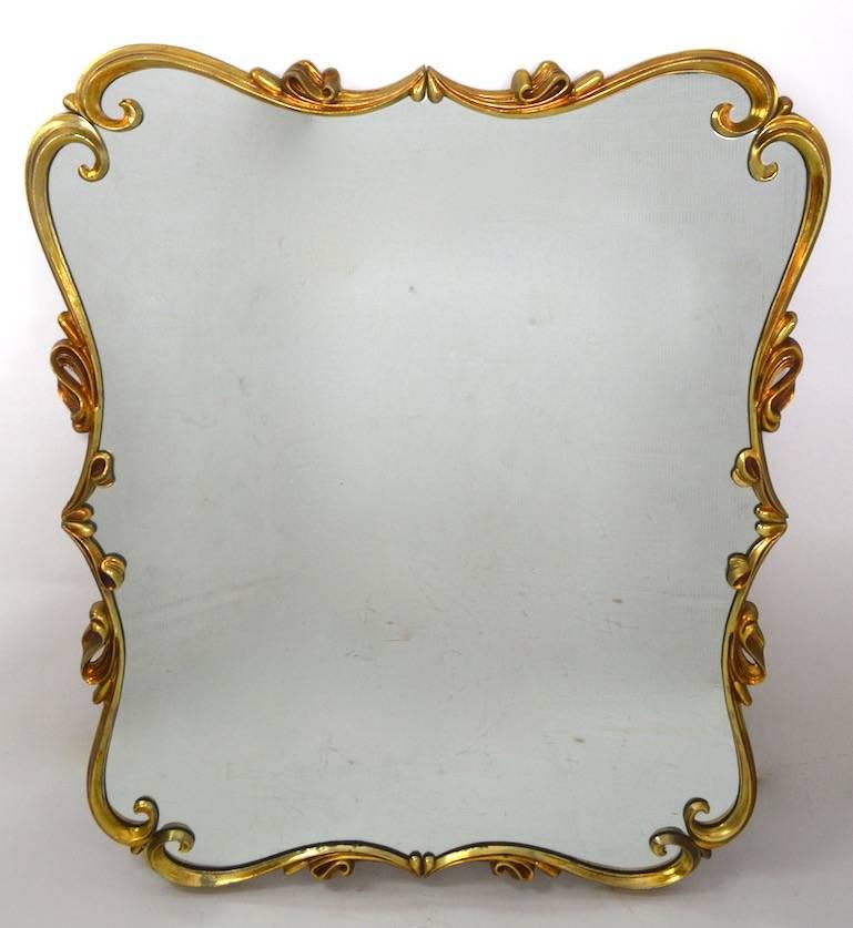 Glamorous Hollywood Regency metal framed plate glass mirror. This example can be hung either vertically or horizontally, the frame is in a faux doré brass plated finish, showing some loss at the lower edge as shown. Frame measure: approximately 1