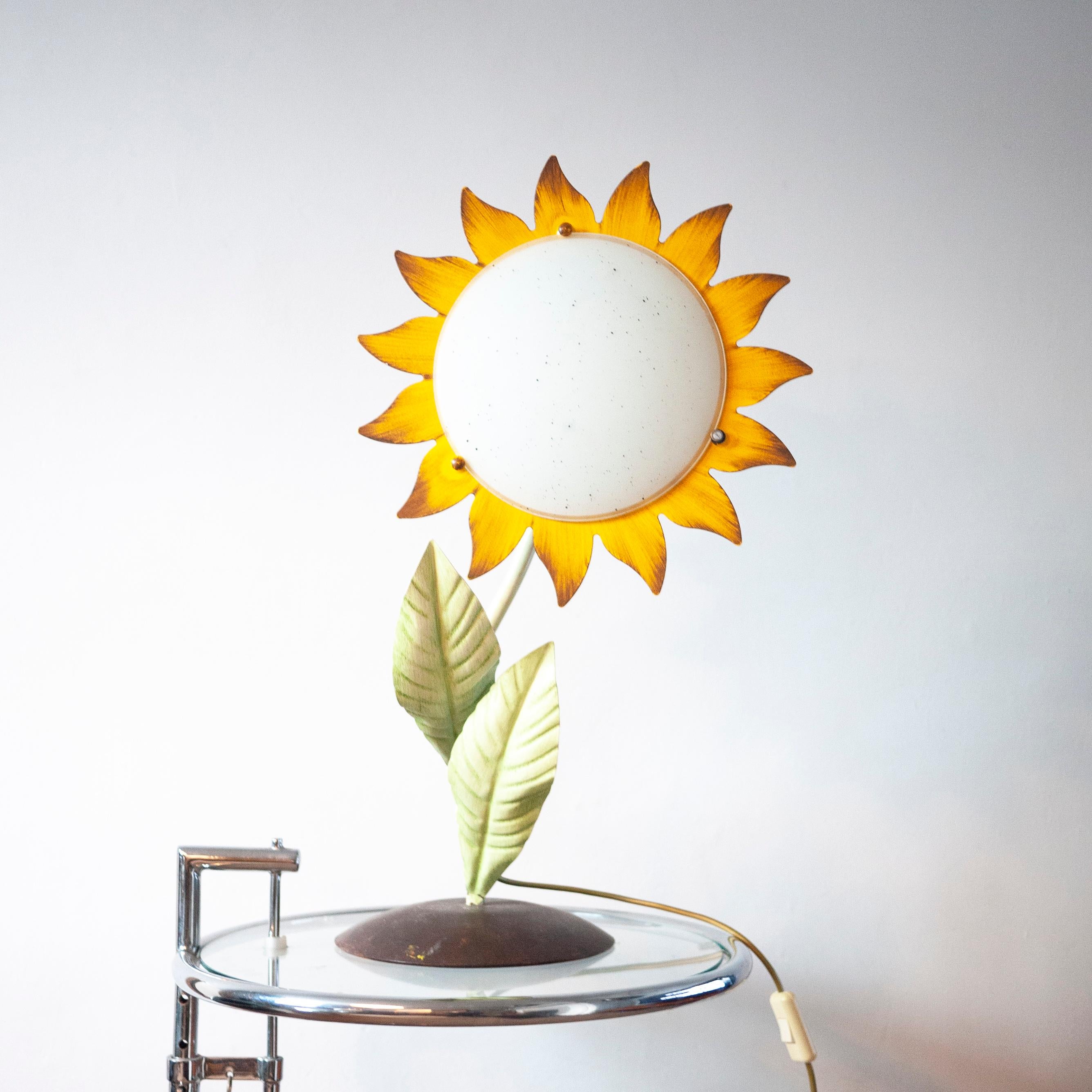 A 1970s hand painted metal sunflower desk lamp. The lamp sits on a round base and has an on/off switch attached to the wire.

Manufacturer - Unknown

Design Period - 1970 to 1979

Country of Manufacture - Italian

Attribution Marks -