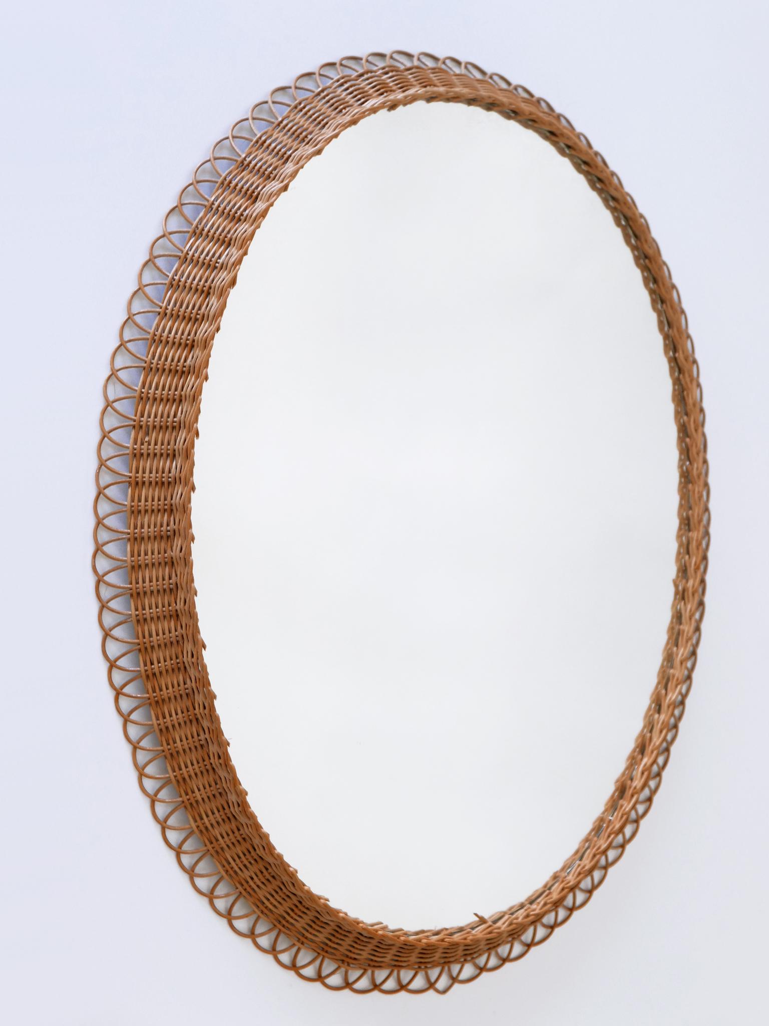 Highly decorative and rare Mid-Century Modern oval wall mirror. 
Manufactured in Germany, 1960s.

Executed in rattan and mirrored glass.

Condition:
Good original vintage condition. Wear consistent with use and age. 

Dimensions with frame:
H 23.23