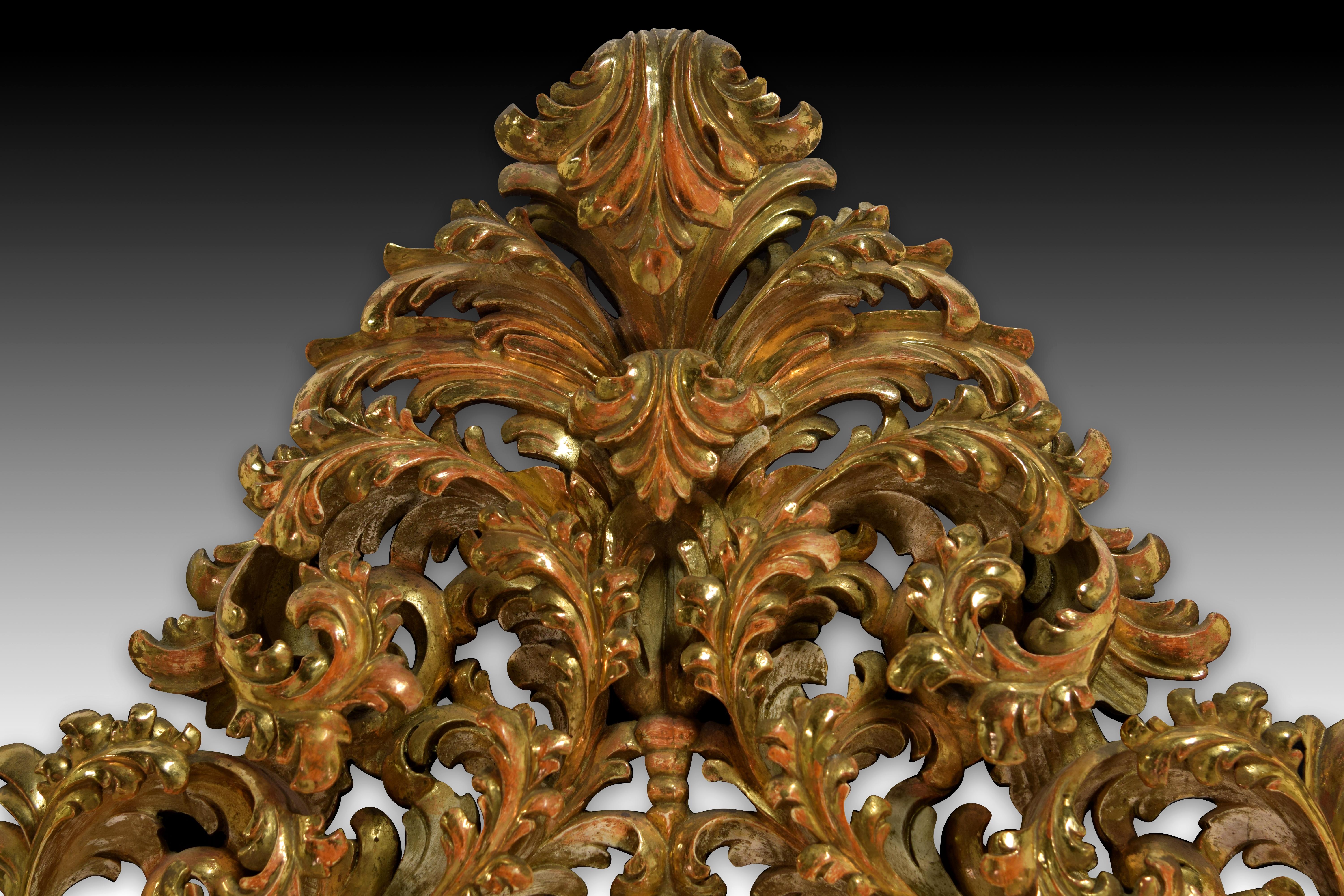Oval mirror. Carved wood, glass. XIX century. 
Oval mirror with a carved and gilded wood frame formed by a simple and smooth molding towards the interior and a complicated but symmetrical openwork composition with a scallop shell and decorative