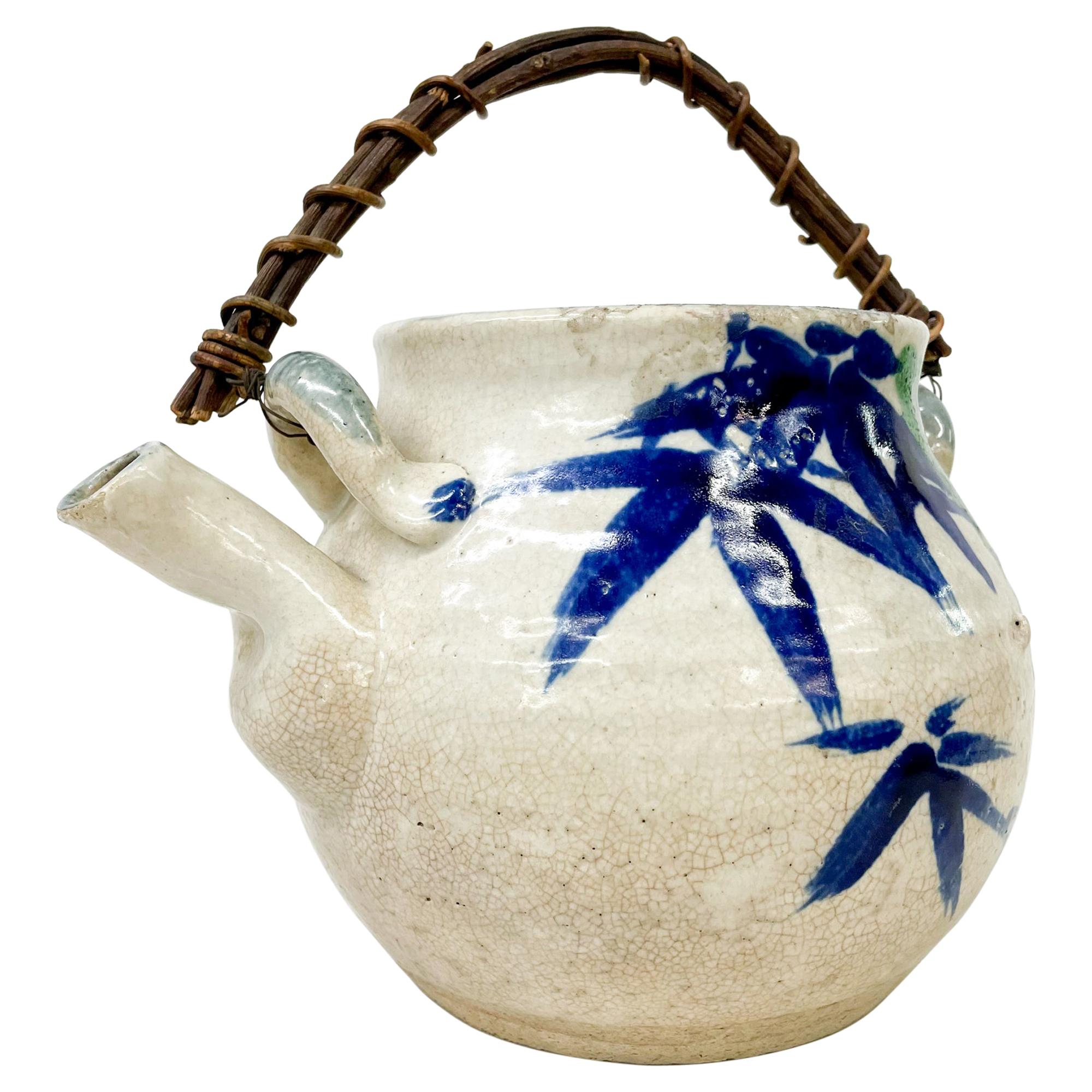 Tea Pot
Decorative Modern Japanese Pottery Tea Pot Hand Decorated Cane Handle.
Made in Japan, Circa the 1970s.
Beautiful round shape. Main color is an off-white with blue tones drawing of bamboo tree. Lovely cane handle. Matching lid.
Signed on the