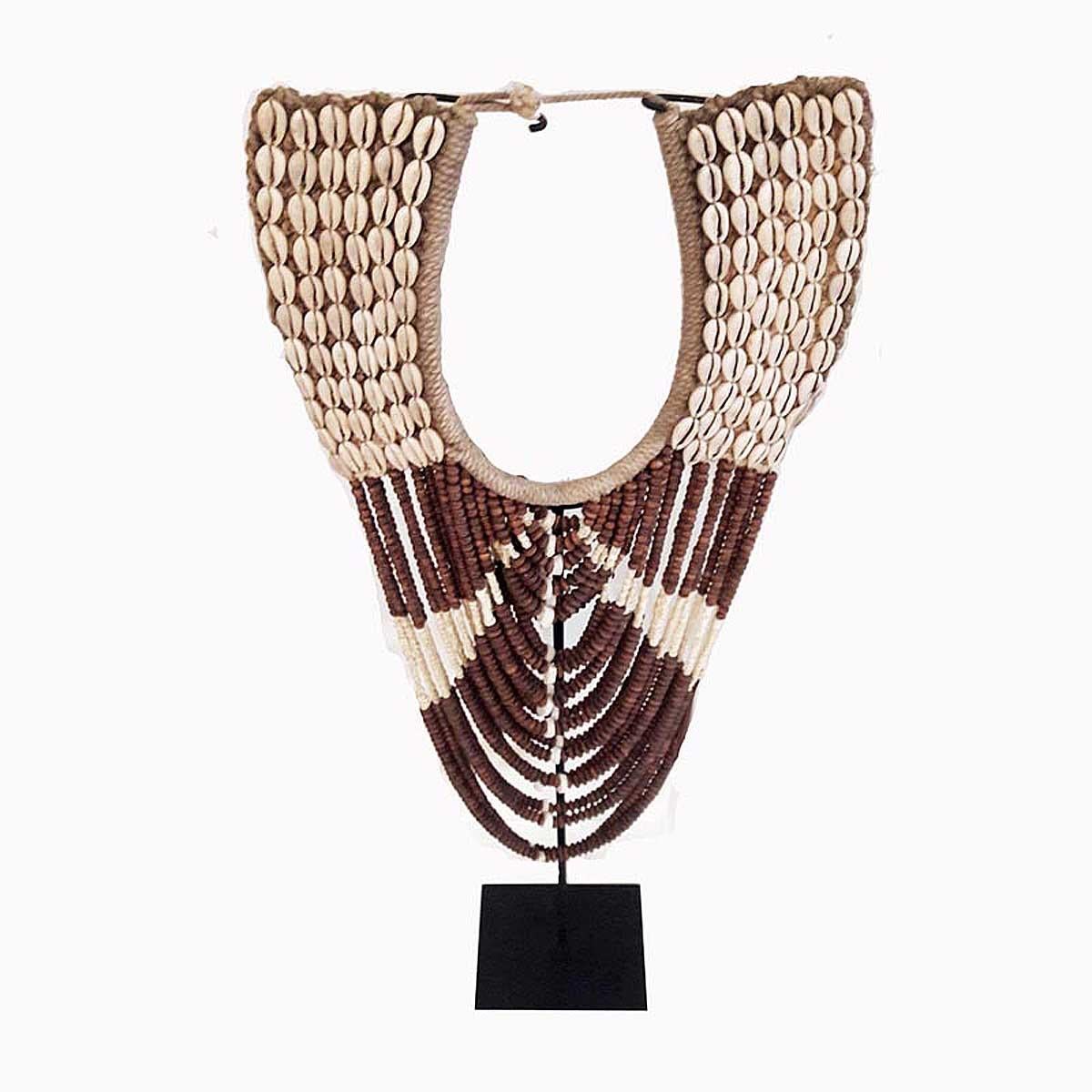 A decorative necklace handcrafted in Bali, mounted on a black metal stand. Puka shell and wood beads, combined with Money Cowry shells and intricately applied on a thick cotton woven canvas.