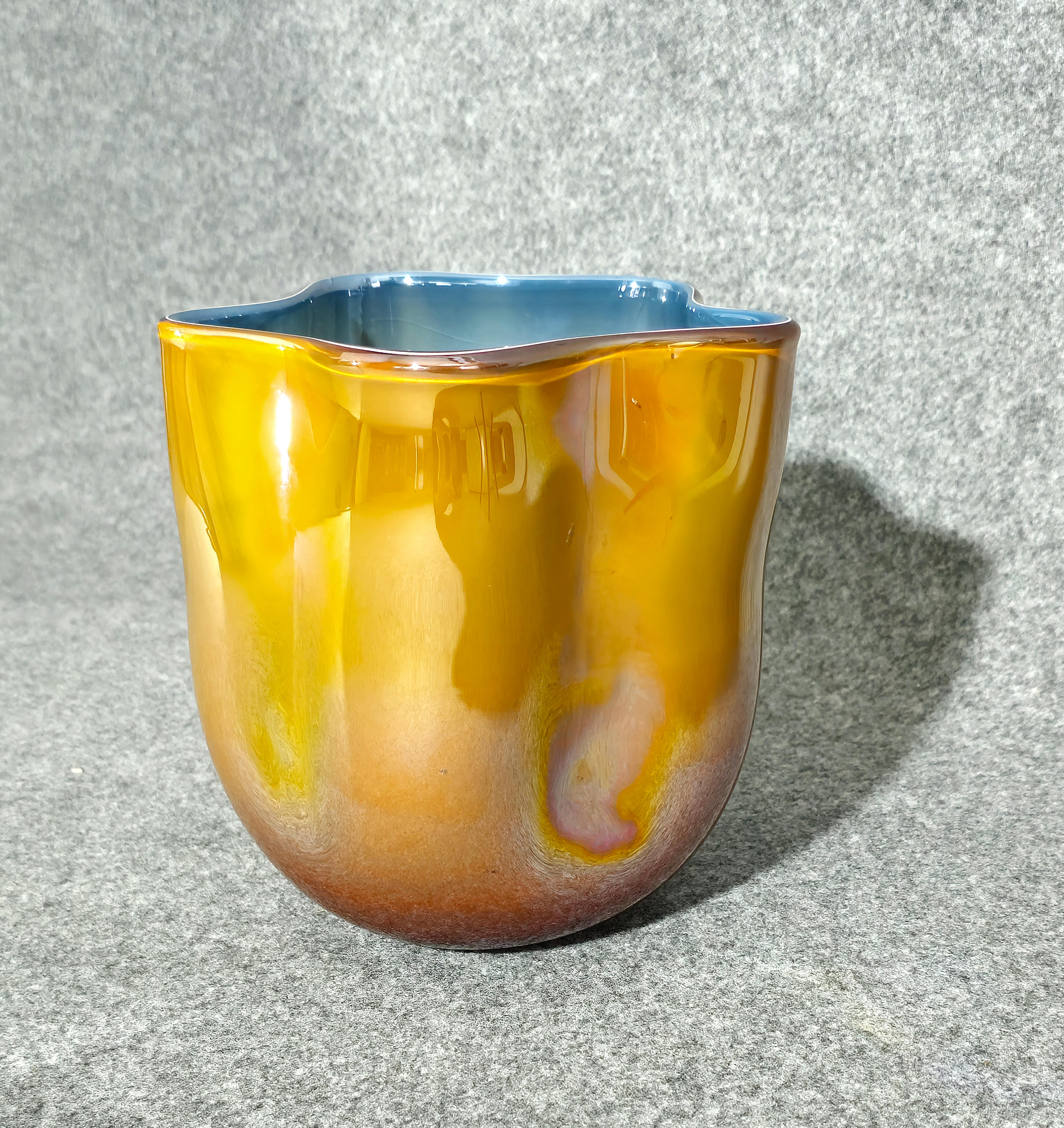 Besondere Vase aus geschichtetem Murano-Glas, bernsteinfarben und blau mit Glanzeffekt. Zylindrischer Körper mit gewellten Wänden, flache gewellte Öffnung, hergestellt in Italien in den 70er Jahren. Leider geben einige Spiegelungen ihm nicht seine