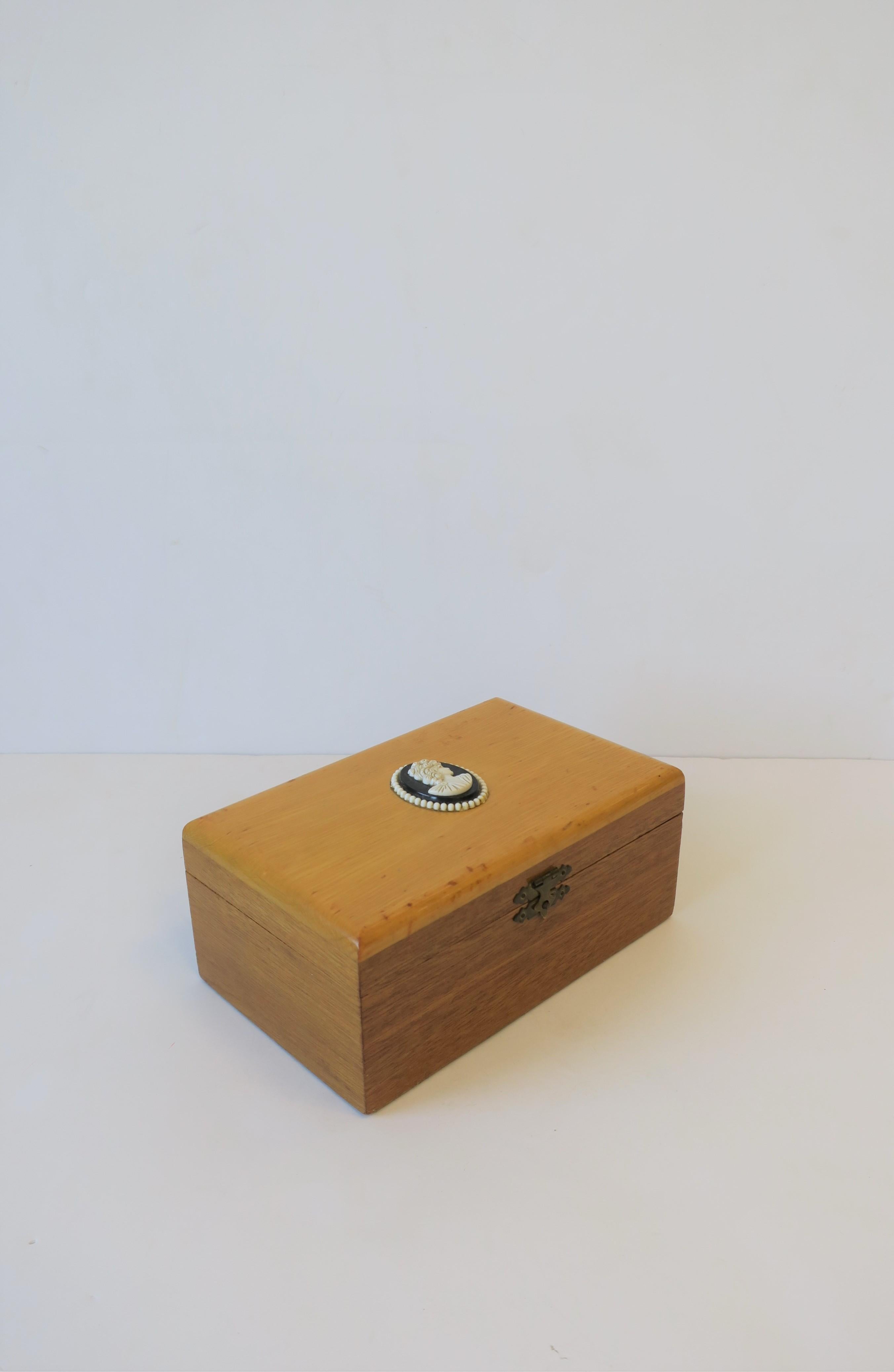 A blonde wood box with black and white Cameo design. Interior is cobalt blue velvet lined. Cameo is a resin or composite material. Box can be decorative or to hold jewelry (as demonstrated) or other items on a desk, vanity, nightstand, etc.