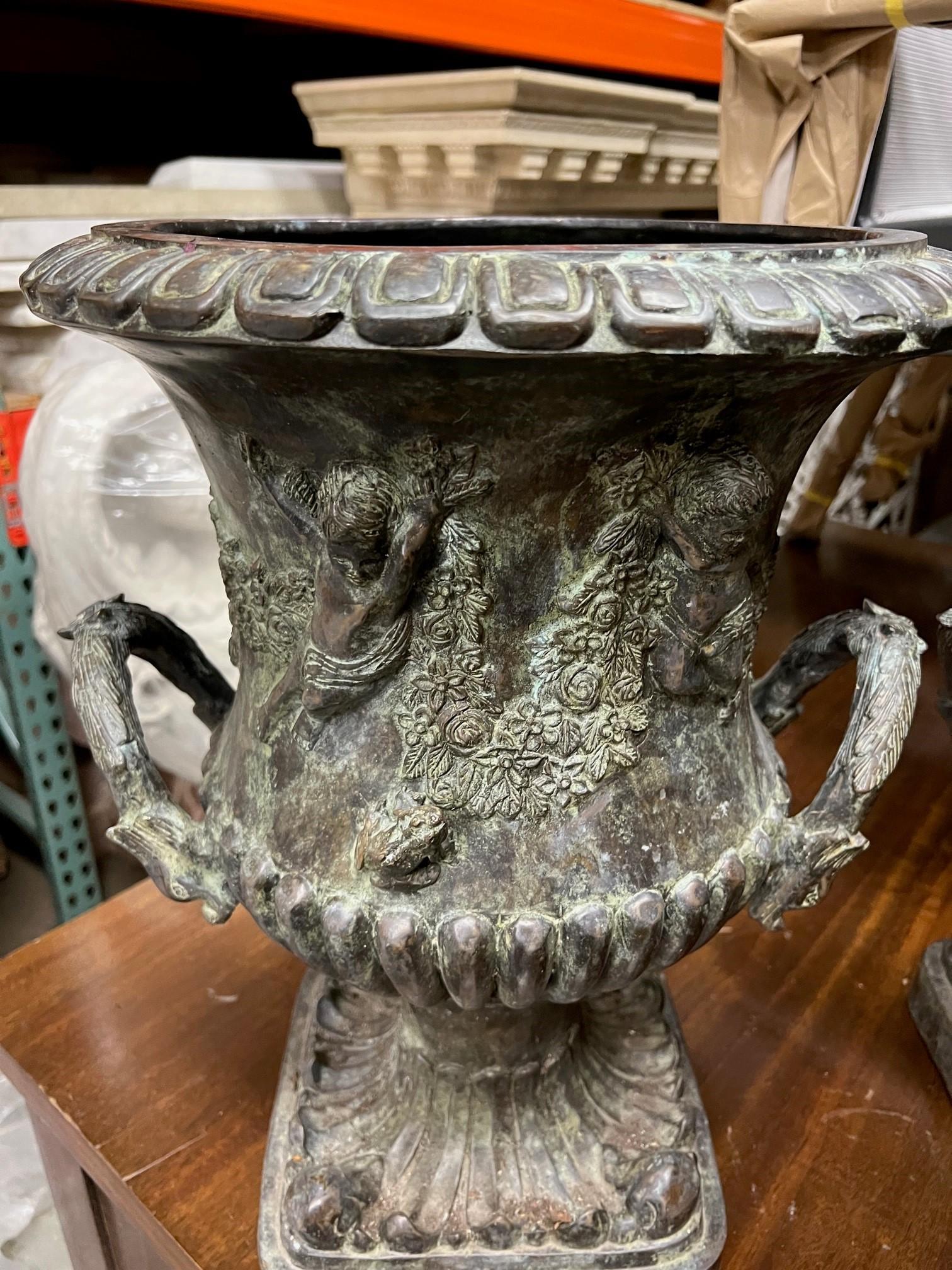 A nice pair of decorative bronze handle urns. The urns have cherubs holding a garland of flowers with a couple of small frogs. Both urns are very beautiful and a great size for plants with a opening 10.5