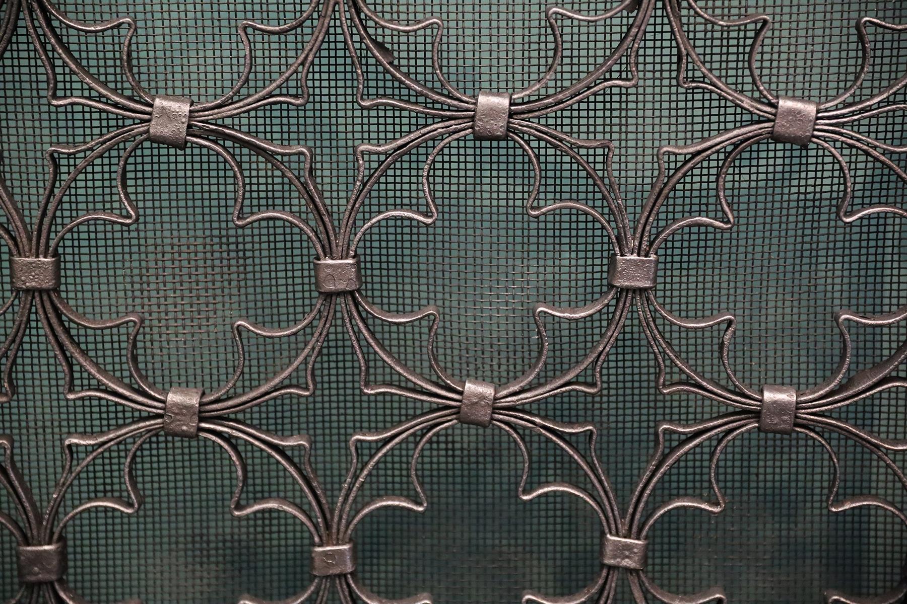 A decorative Quatrefoil fire screen in black-iron finish. The shaped handle with oak leaf and scroll detailing sits above a sturdy wrought-iron frame. Within this the enclosed quatrefoil design sits over the spark mesh sitting on arched scrolled