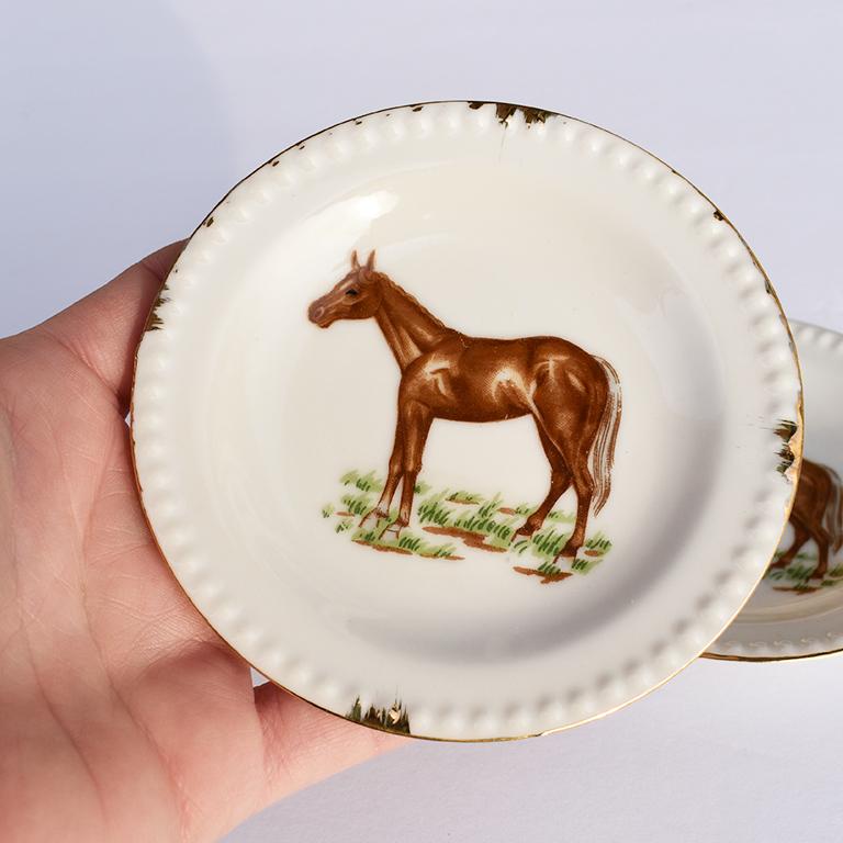 Pair of small round ceramic white porcelain plates with gold trim and horse figures at center. 

Classical and traditional never go out of style. And this pair of lovely plates are no exception. They make for a Classic addition in any traditional