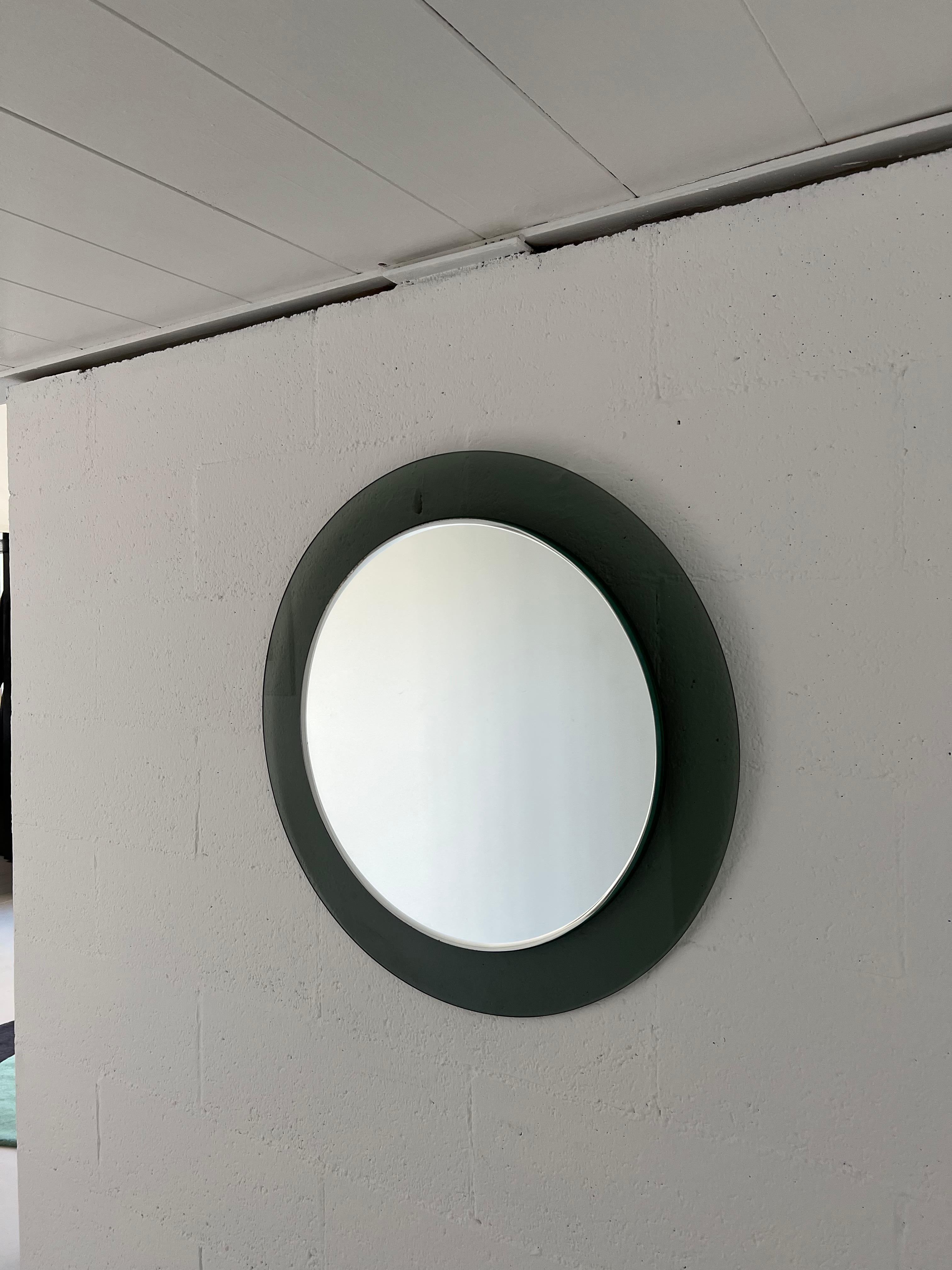 Offered for sale is a timeless, elegant and extremely sleek wall mounted mirror. Round in shape, and entirely made of glass - with a beveled mirror disc attached over a wider circular back in smoked glass, it is minimal yet highly attractive.

It is