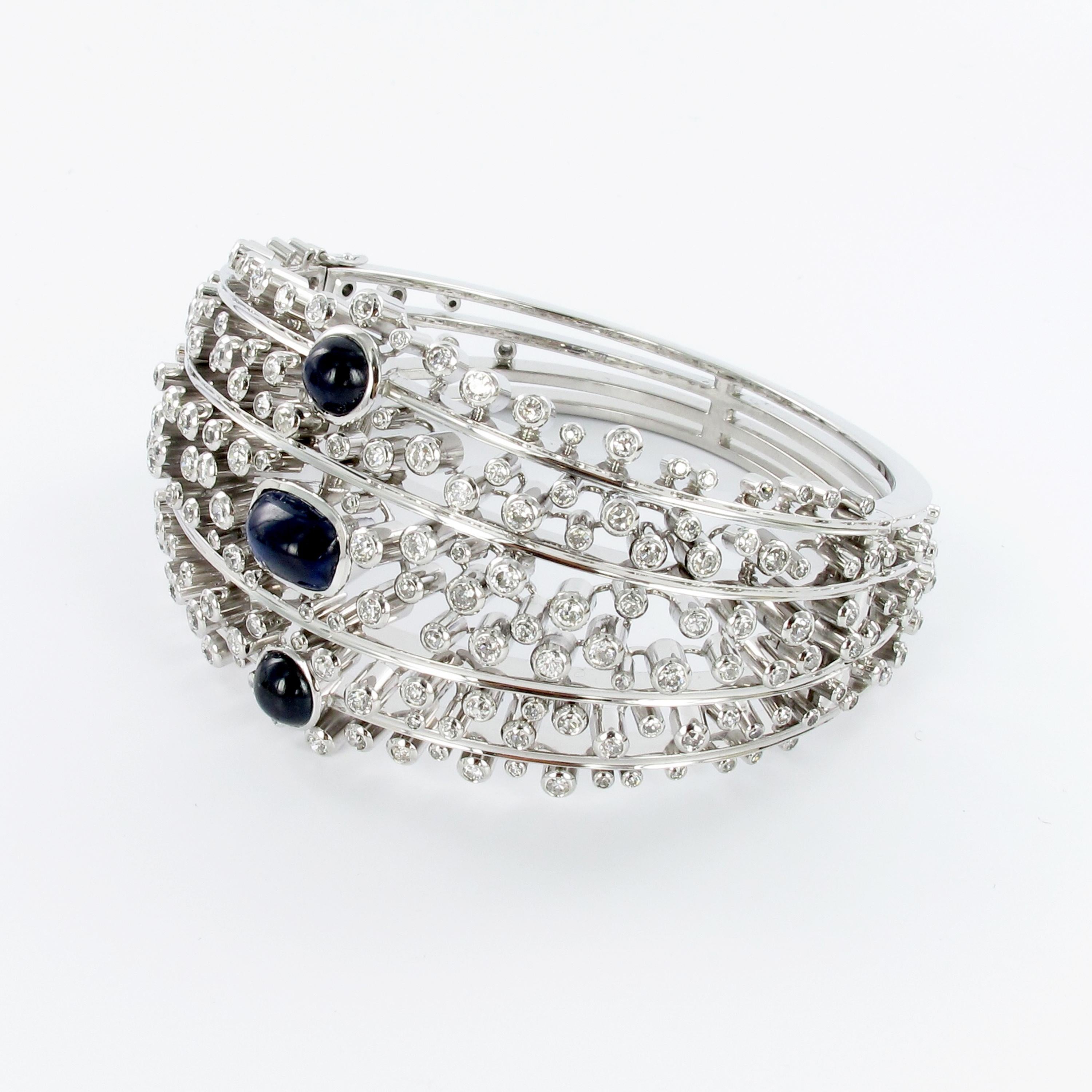 Charming dome shaped bangle in 18K white gold. Set in one line with 3 cabochon cut sapphires totaling approx. 4.00 carats. Further bezel-set with 214 brilliant-cut diamonds of G/H-vs quality totaling 5.00 carats of weight. Box-clasp secured by two