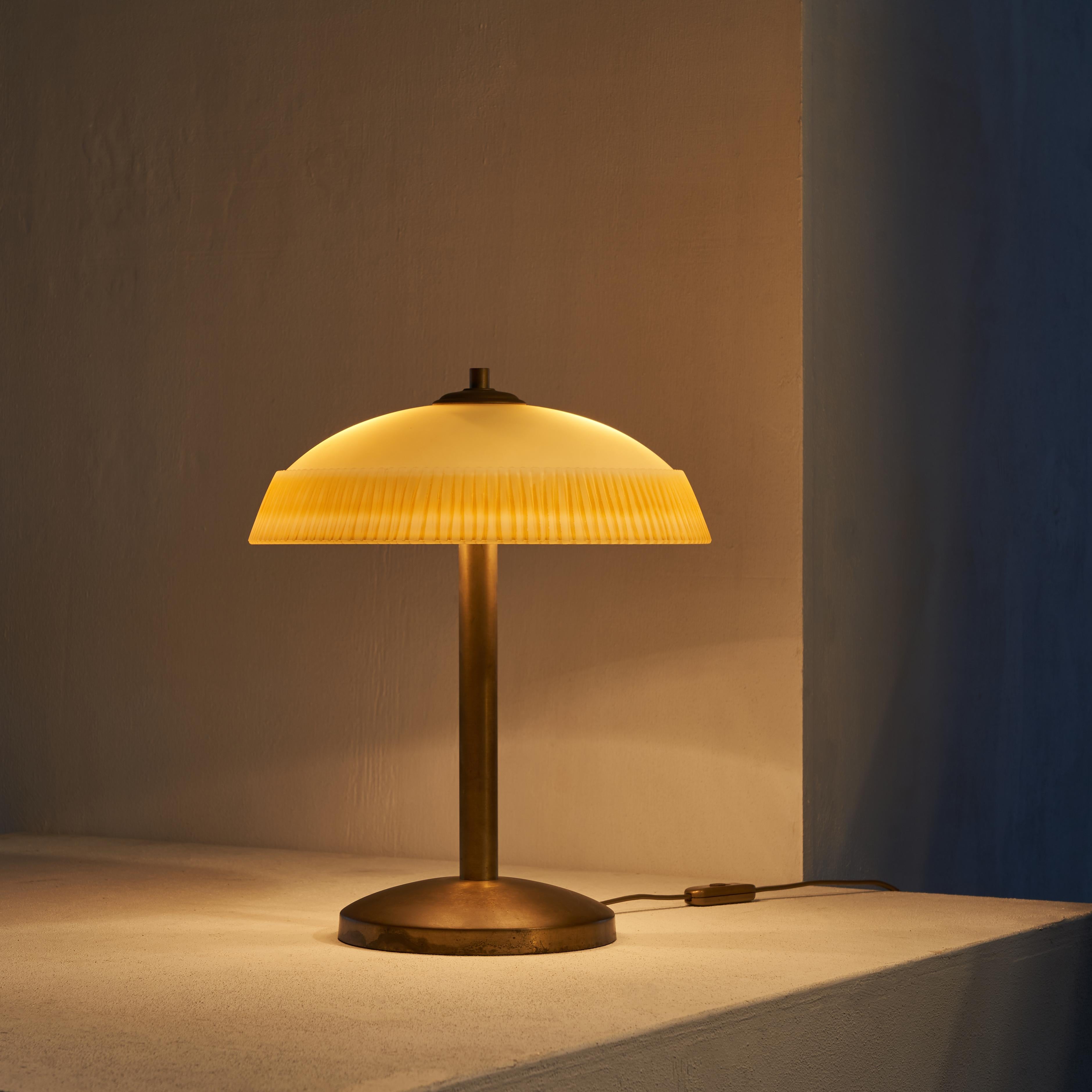 Very delicate and beautiful table lamp with a nicely patinated brass foot and stem. A delightful design with hints to modernism and art deco at the same time. 

The 'Pâte de Verre' glass is very thick and has a decorative ribbed rim and a great