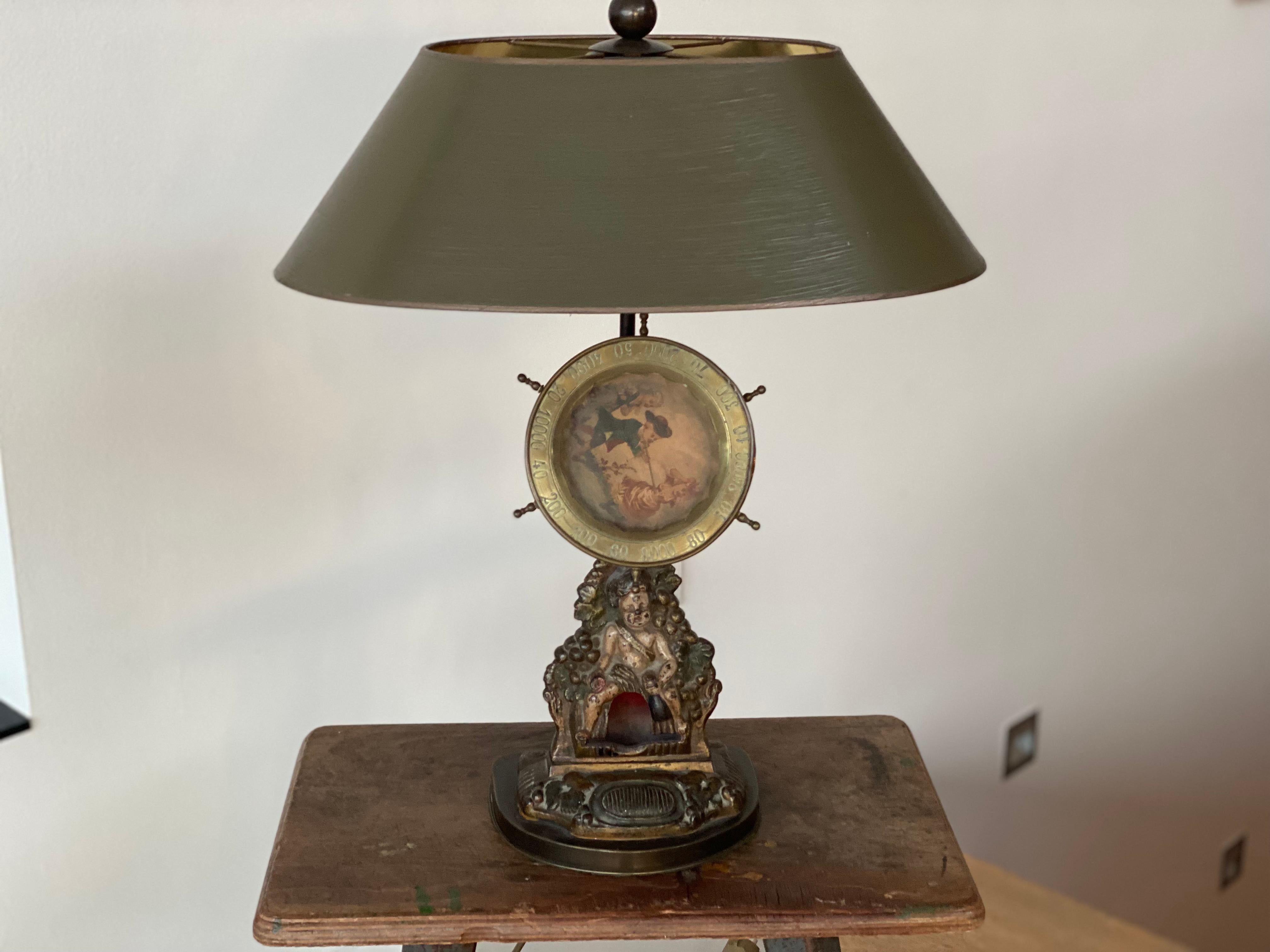 A cast-iron match dispenser serves as a base for this decorative table lamp. The lampshade has been specially made for the lamp and has been hand-painted in a pleasant olive green. The lampshade is lined with gold from the inside, so that the light