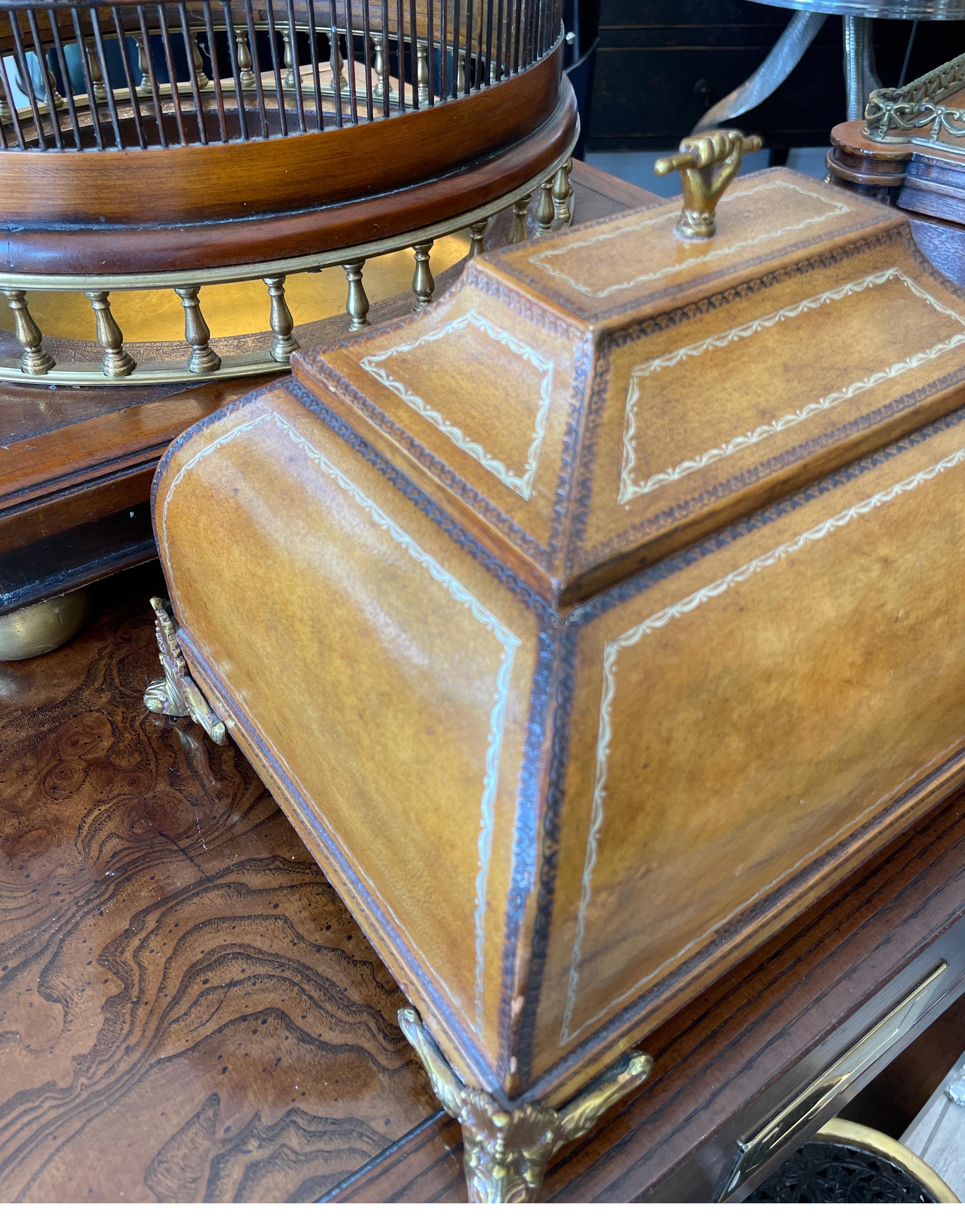 Very decorative tooled leather box with brass feet & trim. Handle is a clasped brass hand. This box opens to a finished interior with ample storage space.