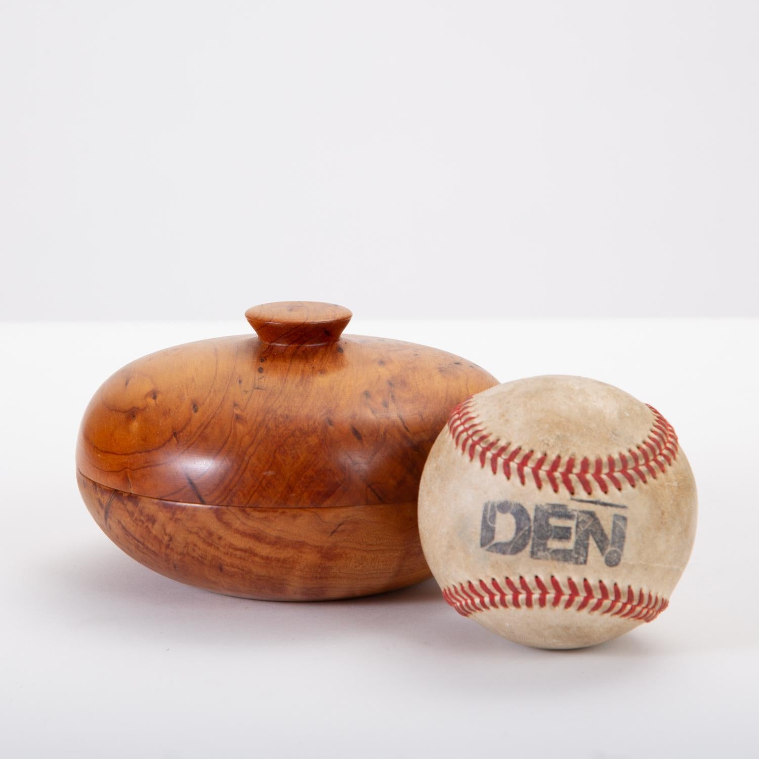 A lathe-turned wooden bowl with a matching lid. Made from Monterey Cypress with a subtle grain pattern and some darker flecking, the bowl is round, with a disc knob on the lid and a lacquer finish. Signed on bottom with artisan’s initials, wood