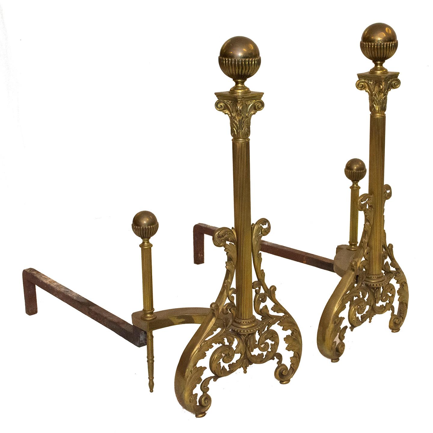These vintage andirons of brass and iron are an attractive pair. The Neoclassical- inspired decorative features include; Corinthian capitals, acanthus leaves, scroll-work, reeded columns, and sphere balls.