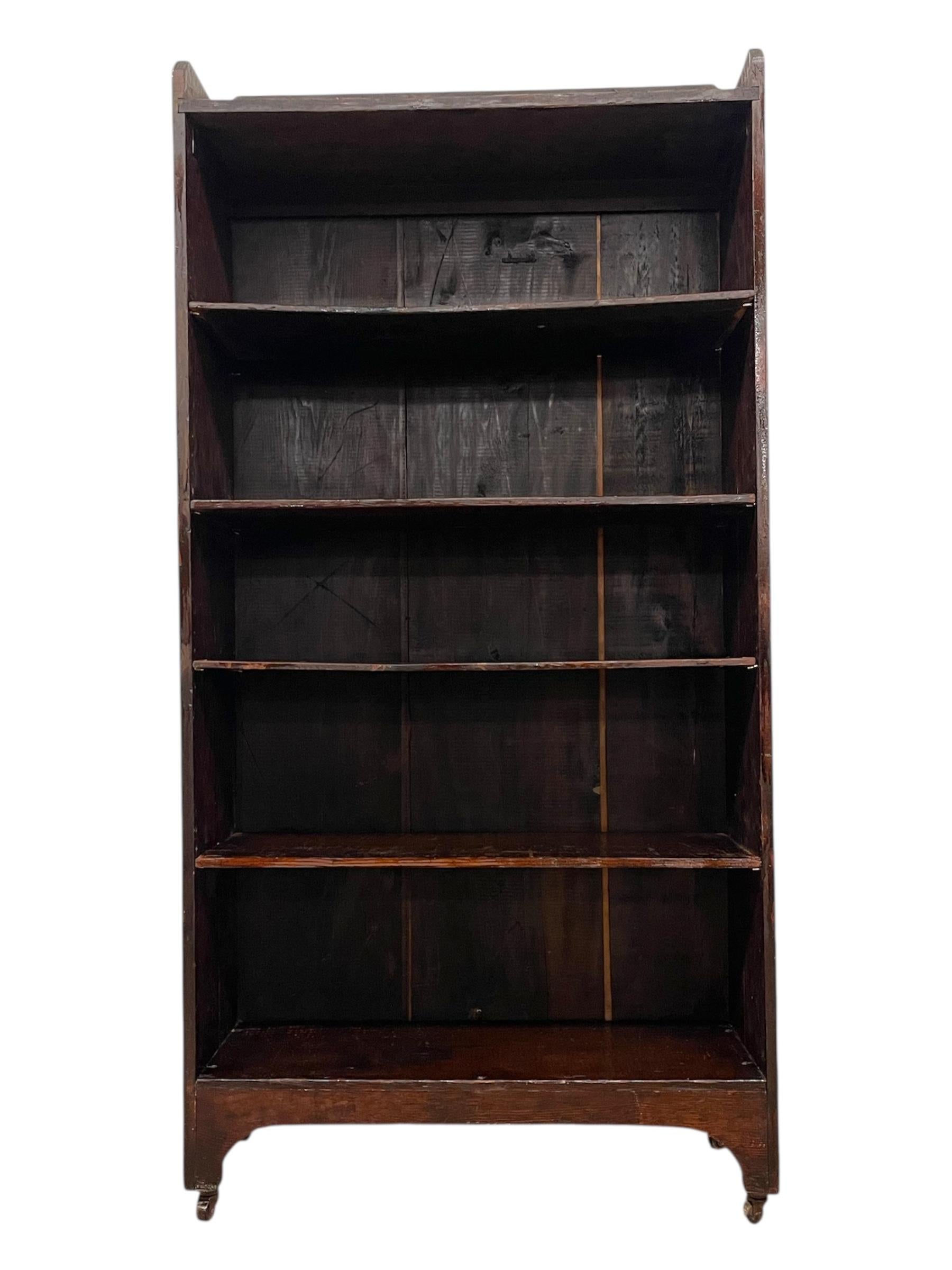 This early 20th-century decorative wooden bookcase features an open-shelf design with five shelves and a raised gallery top, offering generous vertical storage and a warm, timeworn character. Constructed from wood planks, the piece shows visible age