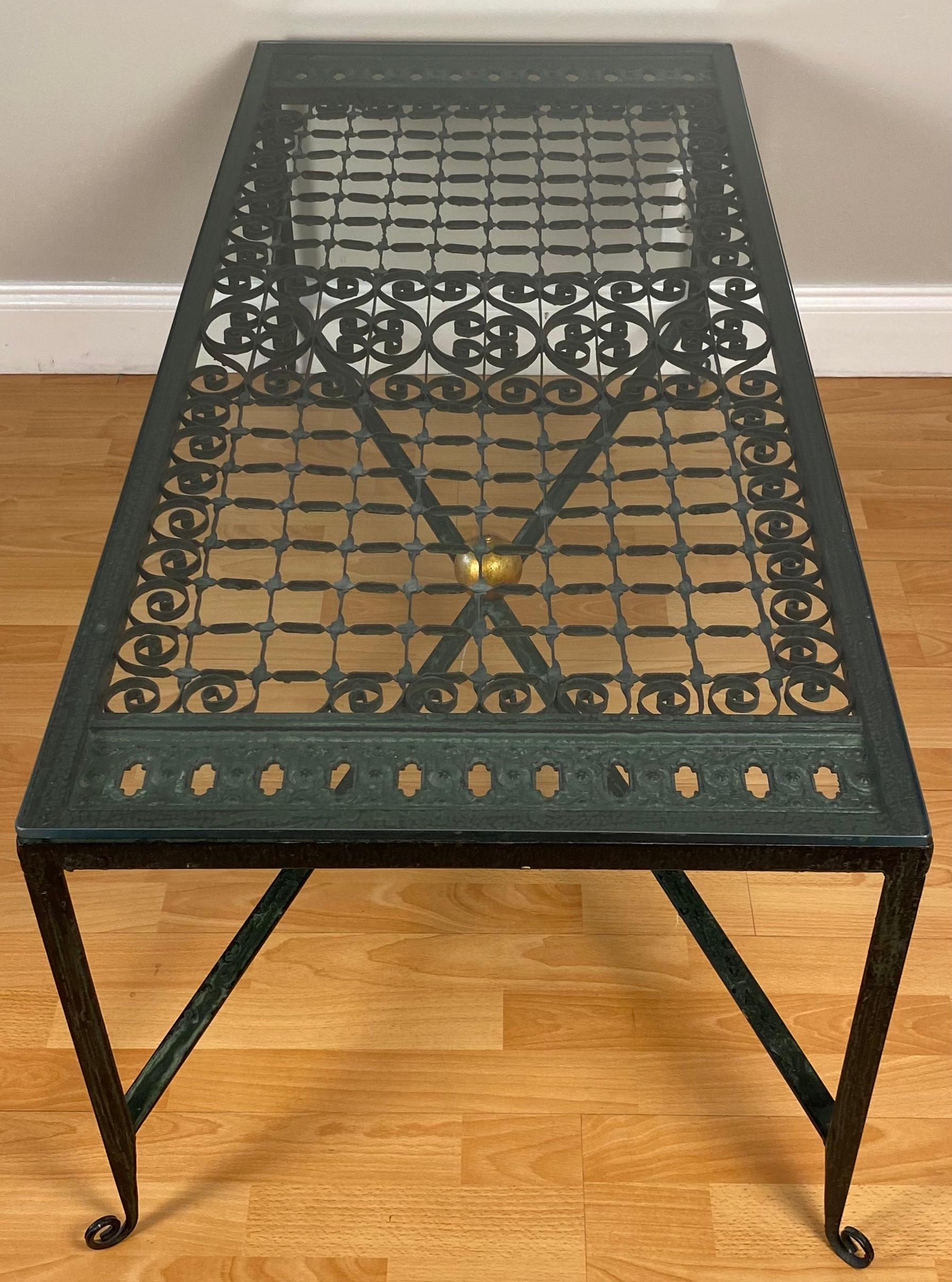 A very good quality mid-century wrought iron cocktail or coffee table with accents in the form of an architectural gate or grille and raised on four legs supported by a top inset with a thick flush-mounted glass. 

Patinated finish. 

Measures: 50