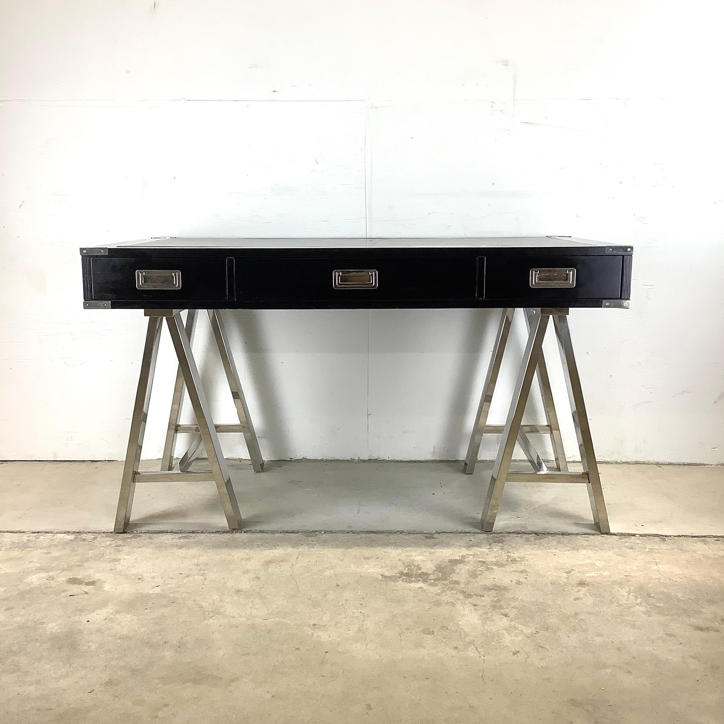 This striking decorator modern campaign style writing desk features an eye catching combination of the black lacquer desk top on polished steel legs. Accented with matching steel hardware and handles the simple yet striking appeal of this large