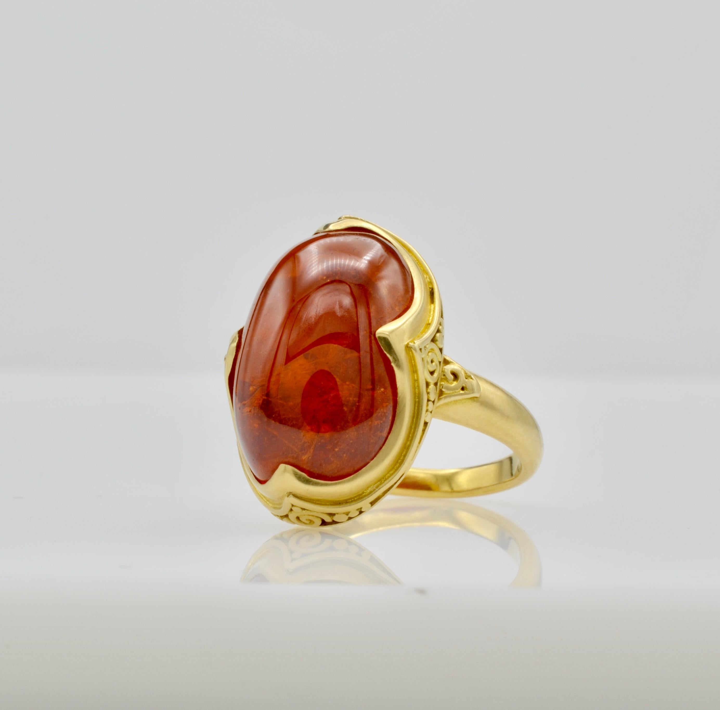 This deep orange tourmaline cabochon Steven Battelle Designed ring is approximately 9.80 ct. and glows from within. The granular 18k gold setting beautifully frames the oval stone. The ring size is 7 1/8 and can be sized to fit your finger.