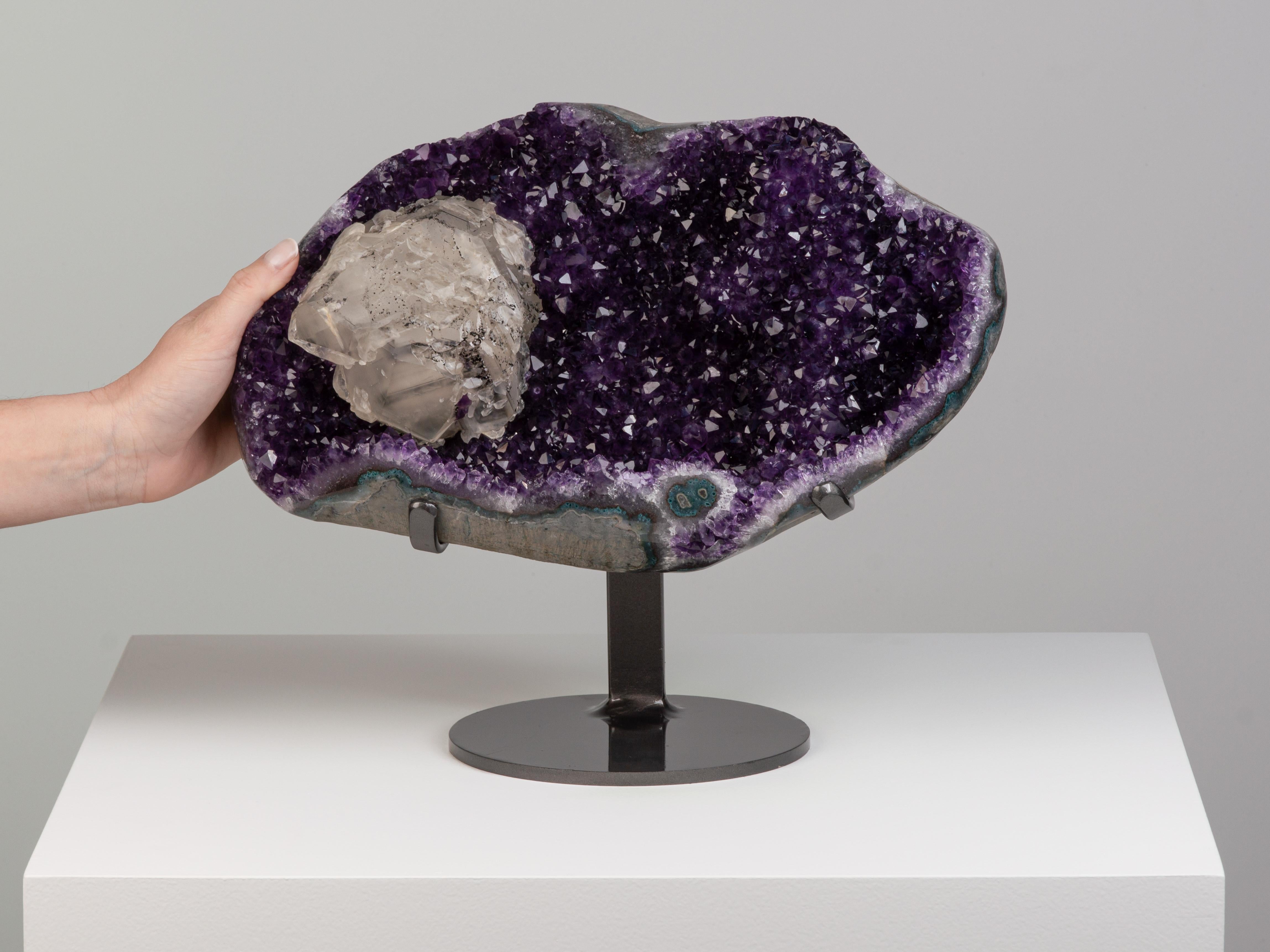 Splendido geode di cristalli di ametista di colore viola intenso. Una grande calcite spicca tra i cristalli, ricoperta da una coltre di ematite nera.

Questo pezzo è stato acquistato in modo legale ed etico direttamente nelle prestigiose miniere