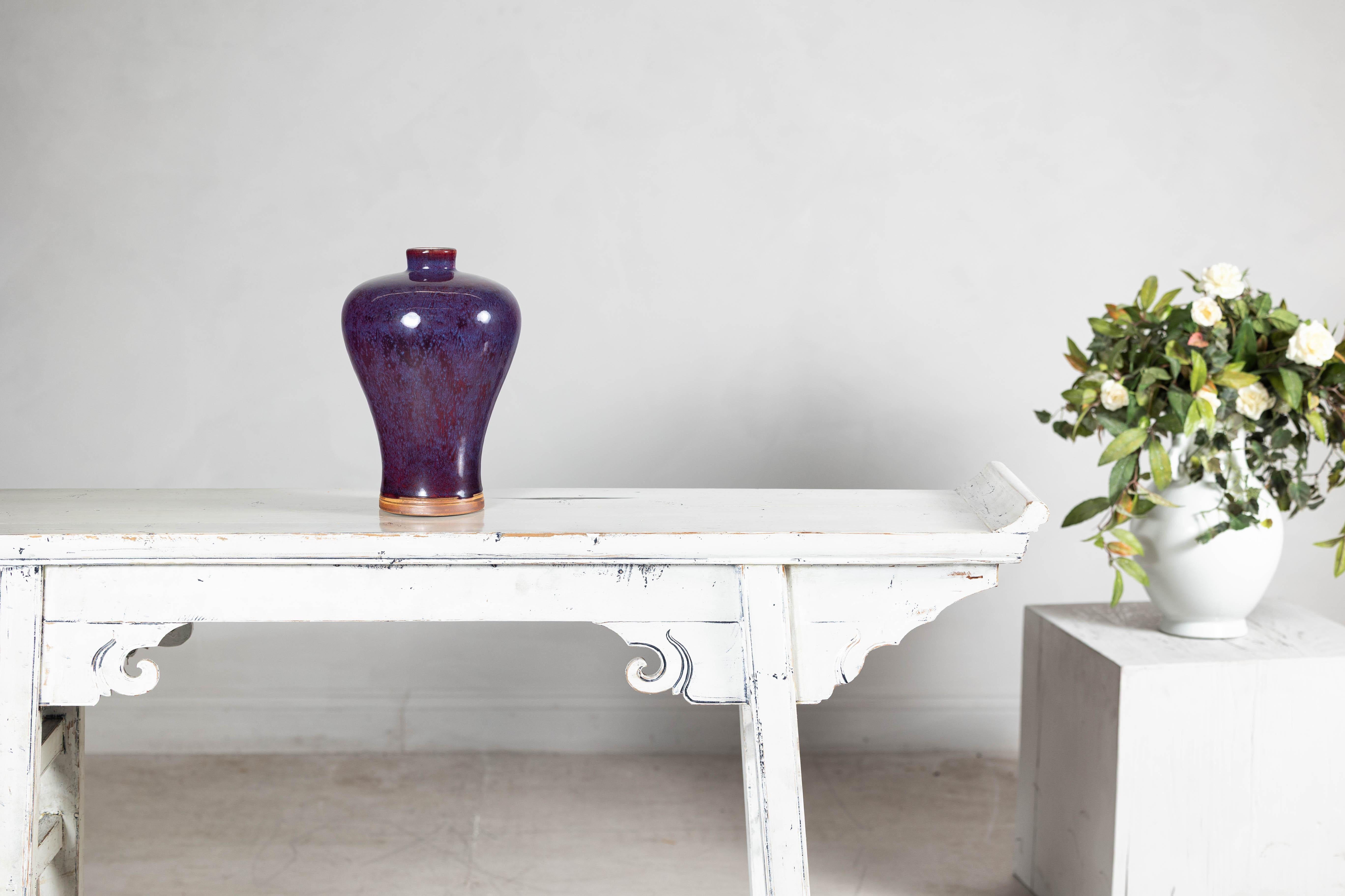 With its elegantly curved silhouette and striking two-tone glaze, this ceramic vase captivates with a deep purple hue that cascades into soft red at the rim. The smooth, high-gloss finish enhances the depth of color, revealing delicate variations