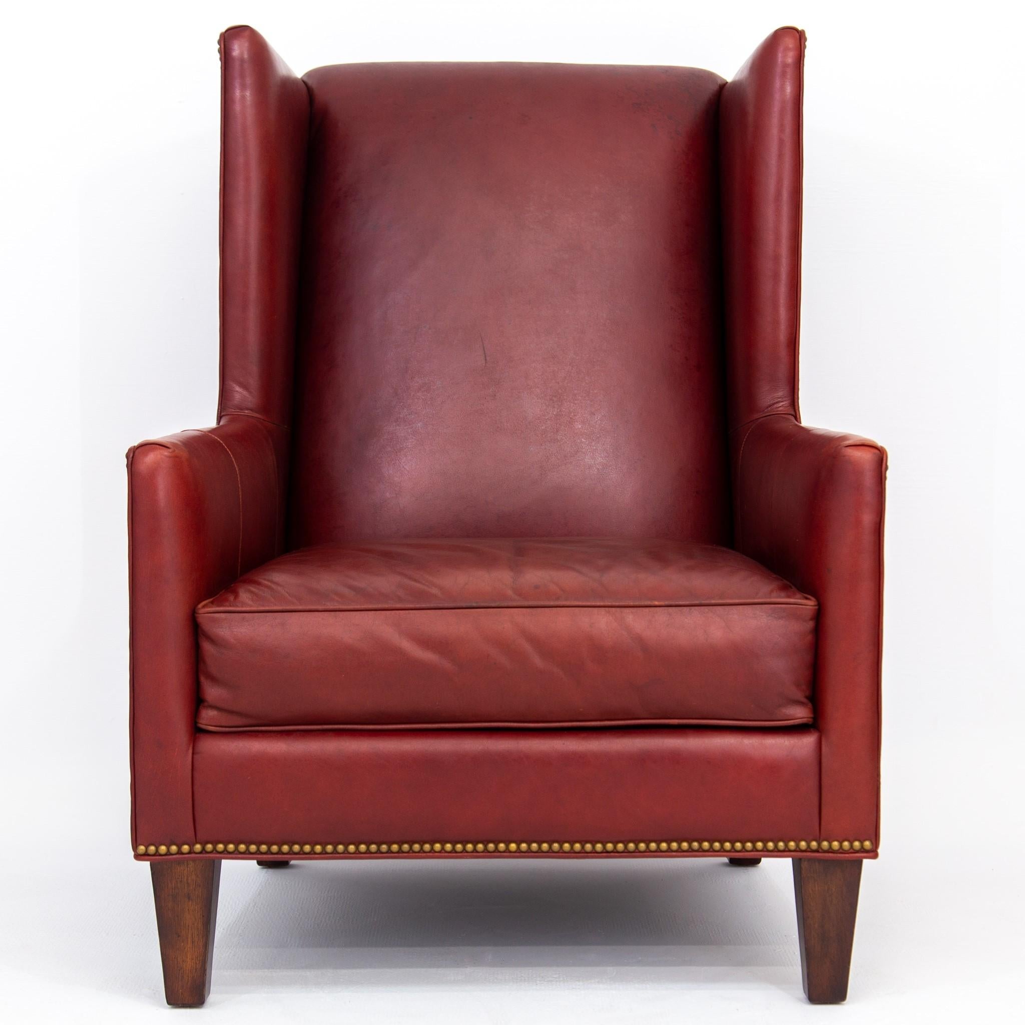 Early 21st-century large angular fireside or wing chair with deep red leather upholstery, brass nailheads and tapered square walnut feet by Massoud. Meticulous craftsmanship with hardwood frame made in the USA. The leather is soft and nicely broken