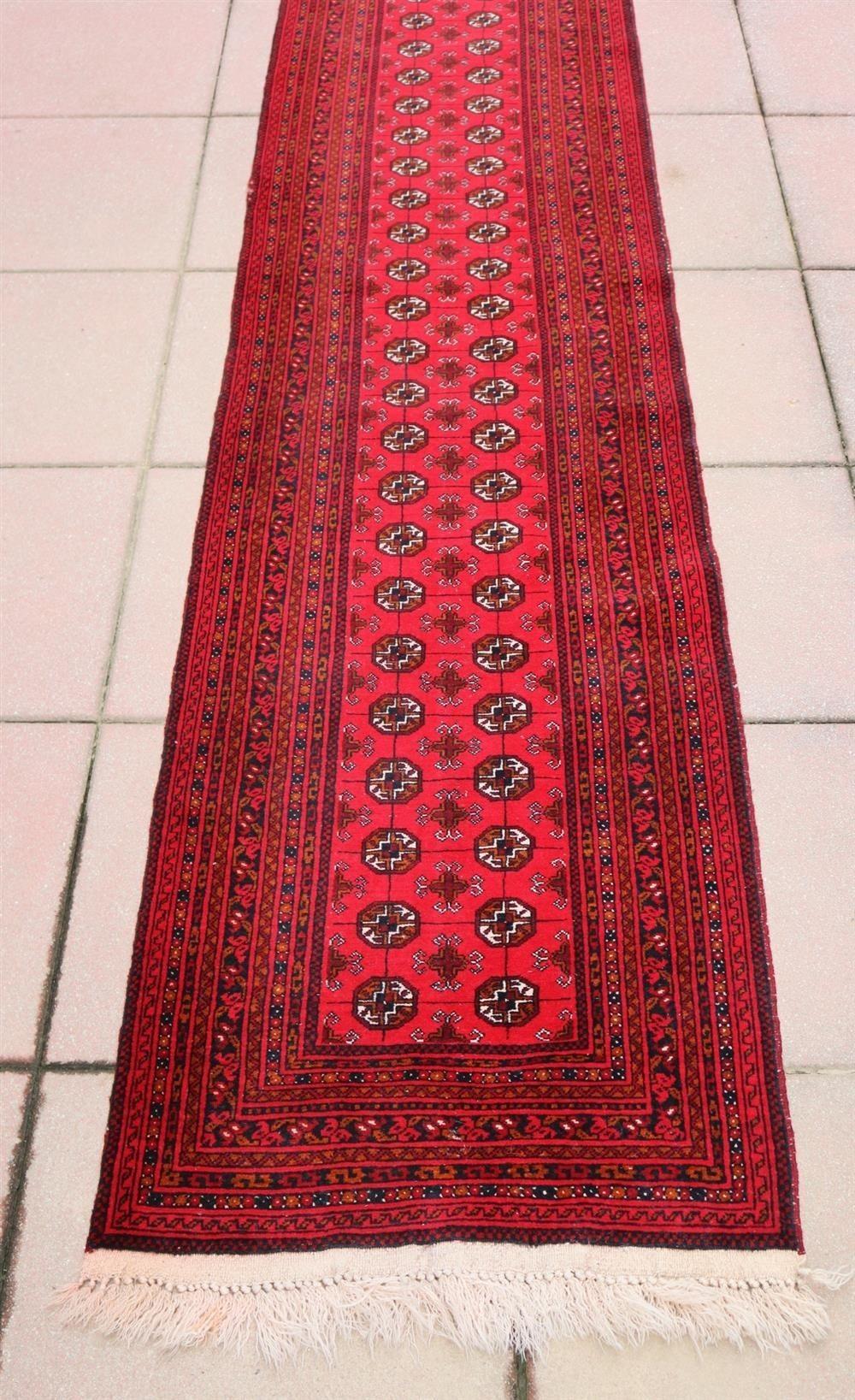 Exceptional Turkestan runner presents a stunning display of deep red tones and traditional geometric medallions adorning its surface. The deep red hues are complemented by accents of vibrant blue, warm orange, and crisp white tones, creating a