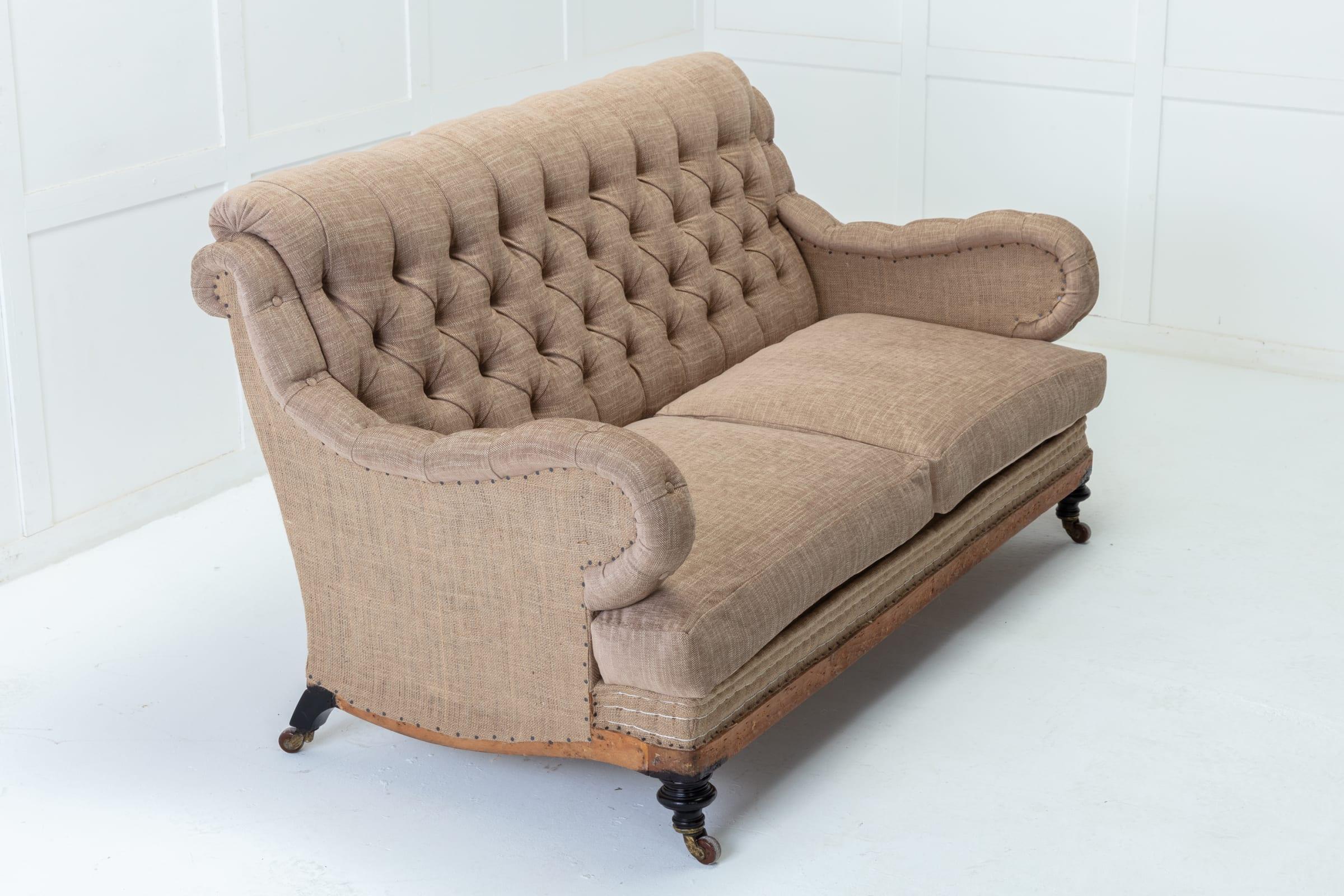 A tailored two seater button-back couch with rolled arms and deep seat, in the fashion of Howard and Sons, on turned legs with brass castors. Fully stripped back and freshly reupholstered in a deconstructed manner in hand-stitched putty colored jute