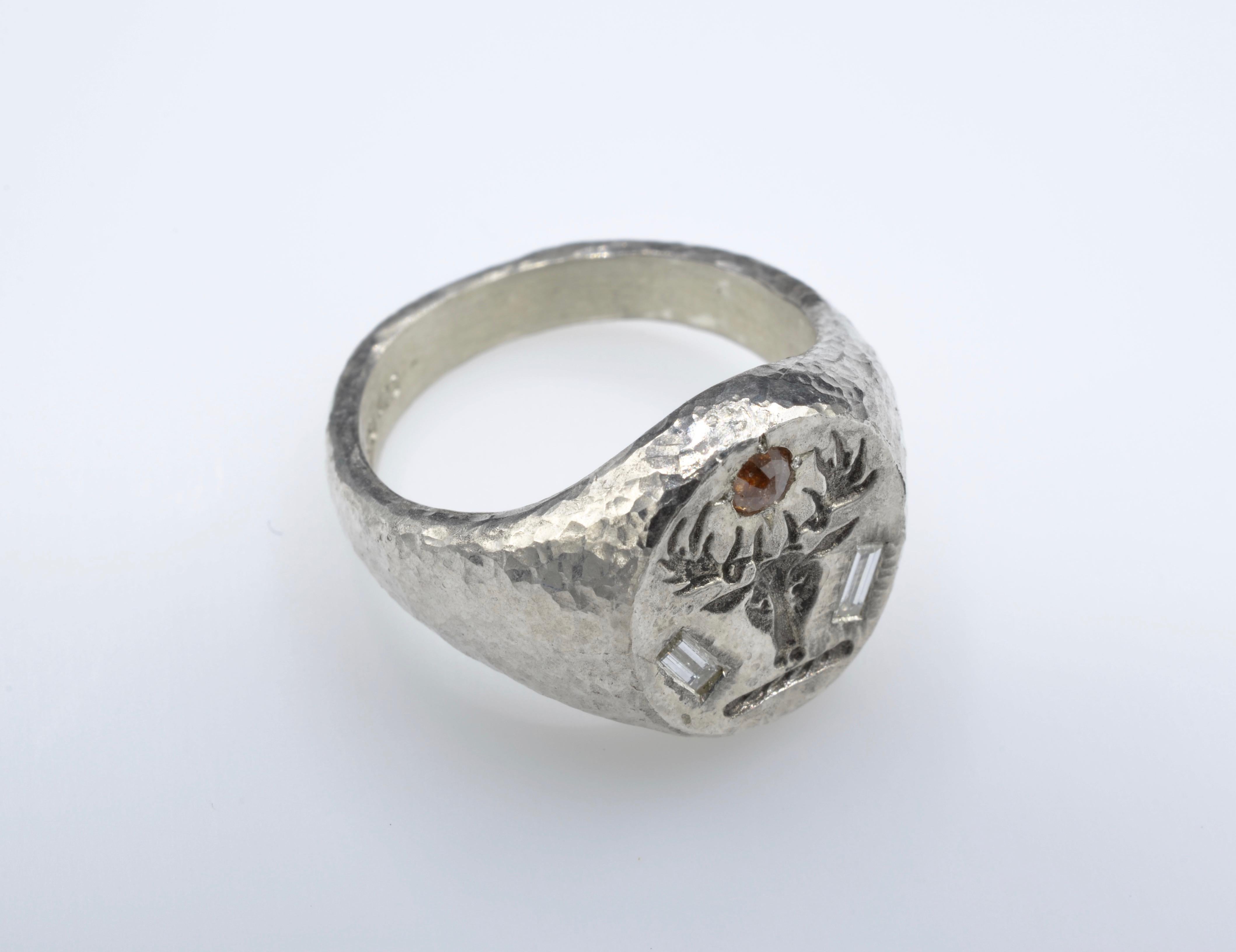 Traditionelle Form eines Siegelrings, mit der Besonderheit der gehämmerten Textur in Silber und mit Diamanten besetzt. Die beiden Baguette-Diamanten von je 0,10 Karat an der Seite des Hirschkopfes verleihen dem Ring einen modernen Look. Das Oberteil