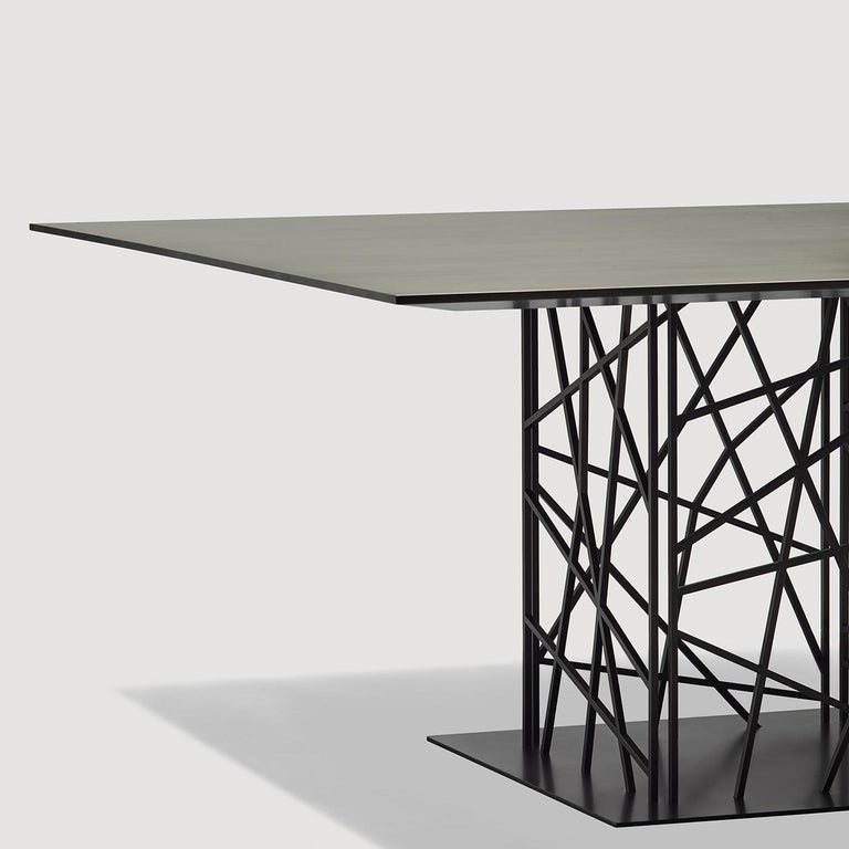 A striking geometrical weave is the defining element of this superb dining table's base structure. Crafted of steel, the base is composed of four sheets of different textures obtained with a laser-cut work. The splendid rectangular top of this piece