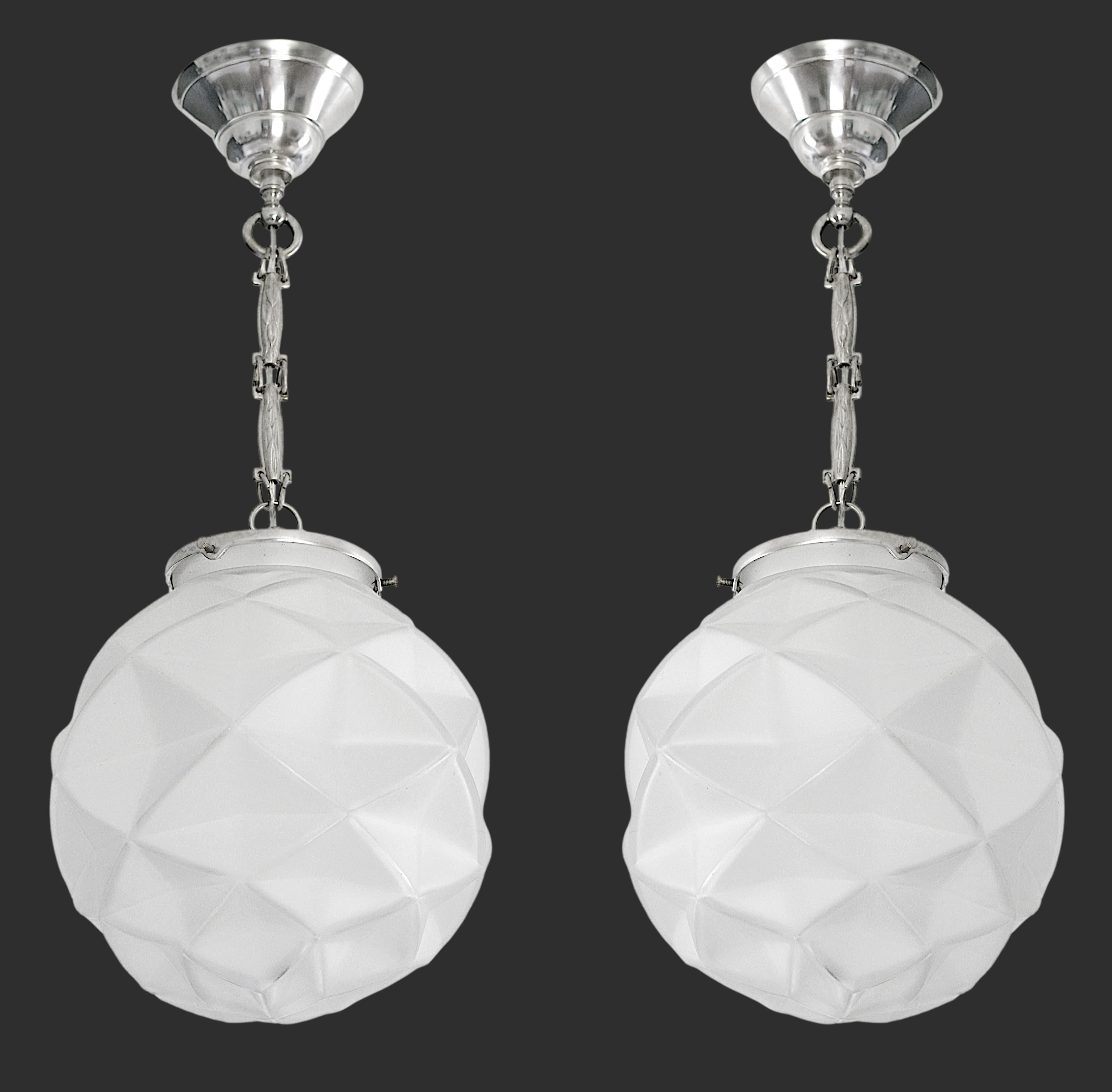 Pair of French Art Deco pendants chandeliers by DEGUE (Compiegne), France, ca. 1930. White frosted glass shade hung at its nickel plated fixture. Stamped brass links. Each - Height: 19.7