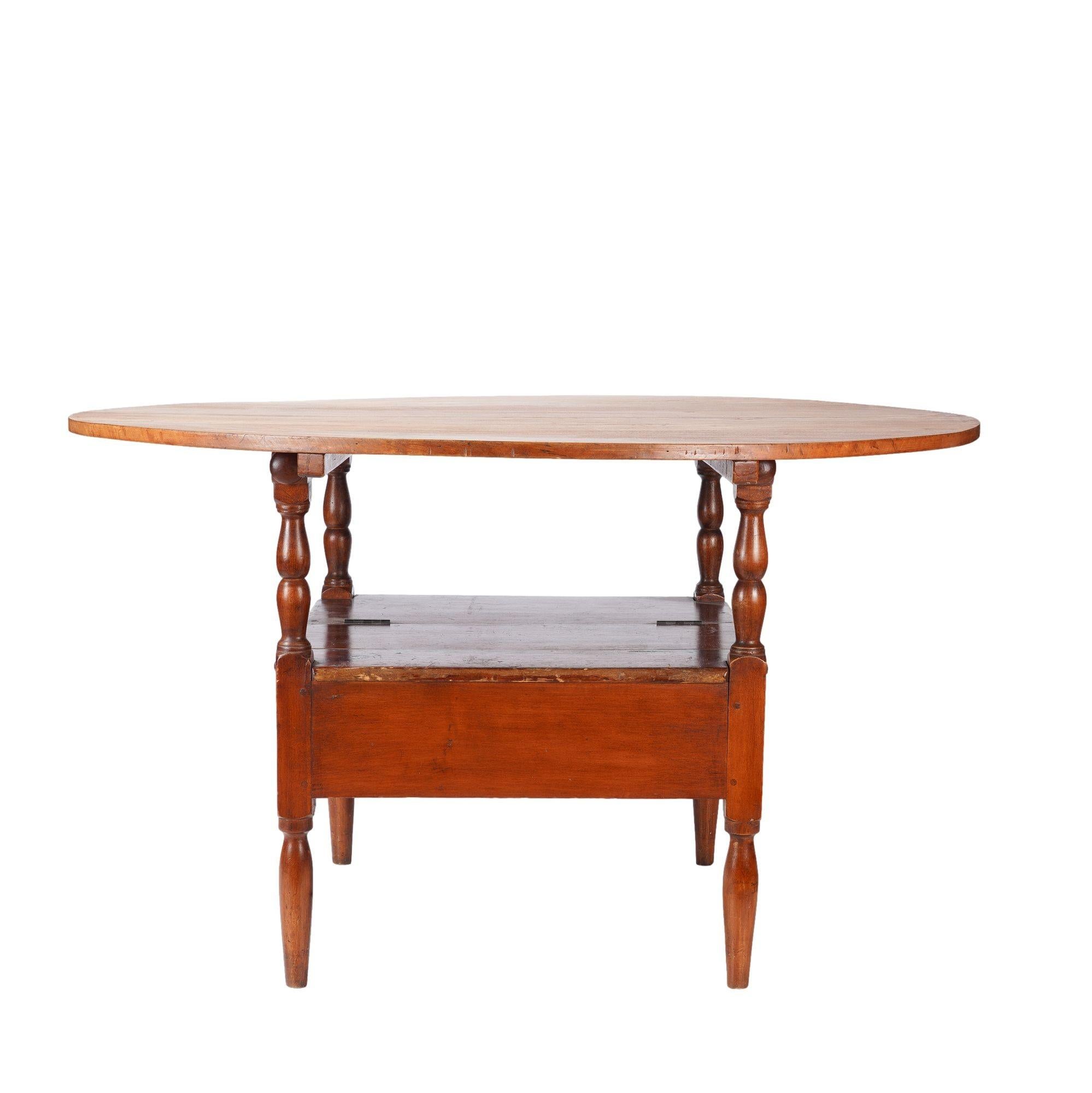 Delaware Valley metamorphic Monk's Bench tilt top settle base table in cherry wood. The two board top is attached to the bearer rails with two removable wood pegs, and the bearer rails are supported by four turned legs. The legs are joined by a