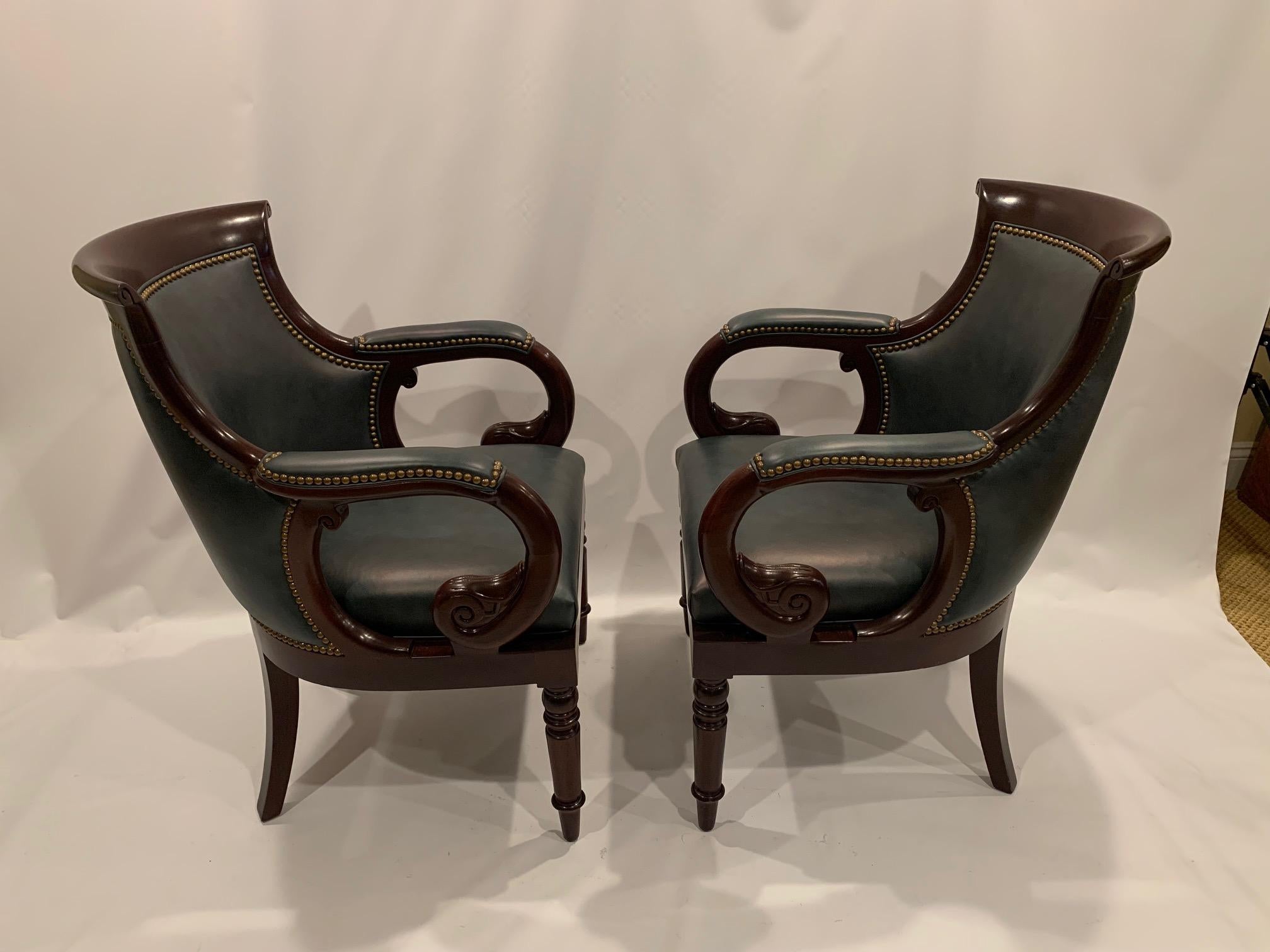 A richly elegant pair of barrel back shaped club chairs having mahogany frames, curved arms and turned legs. The warm brown of the wood is complimented by the sumptuous blue leather. Brass nailheads add an exquisite icing to the cake. Chairs are