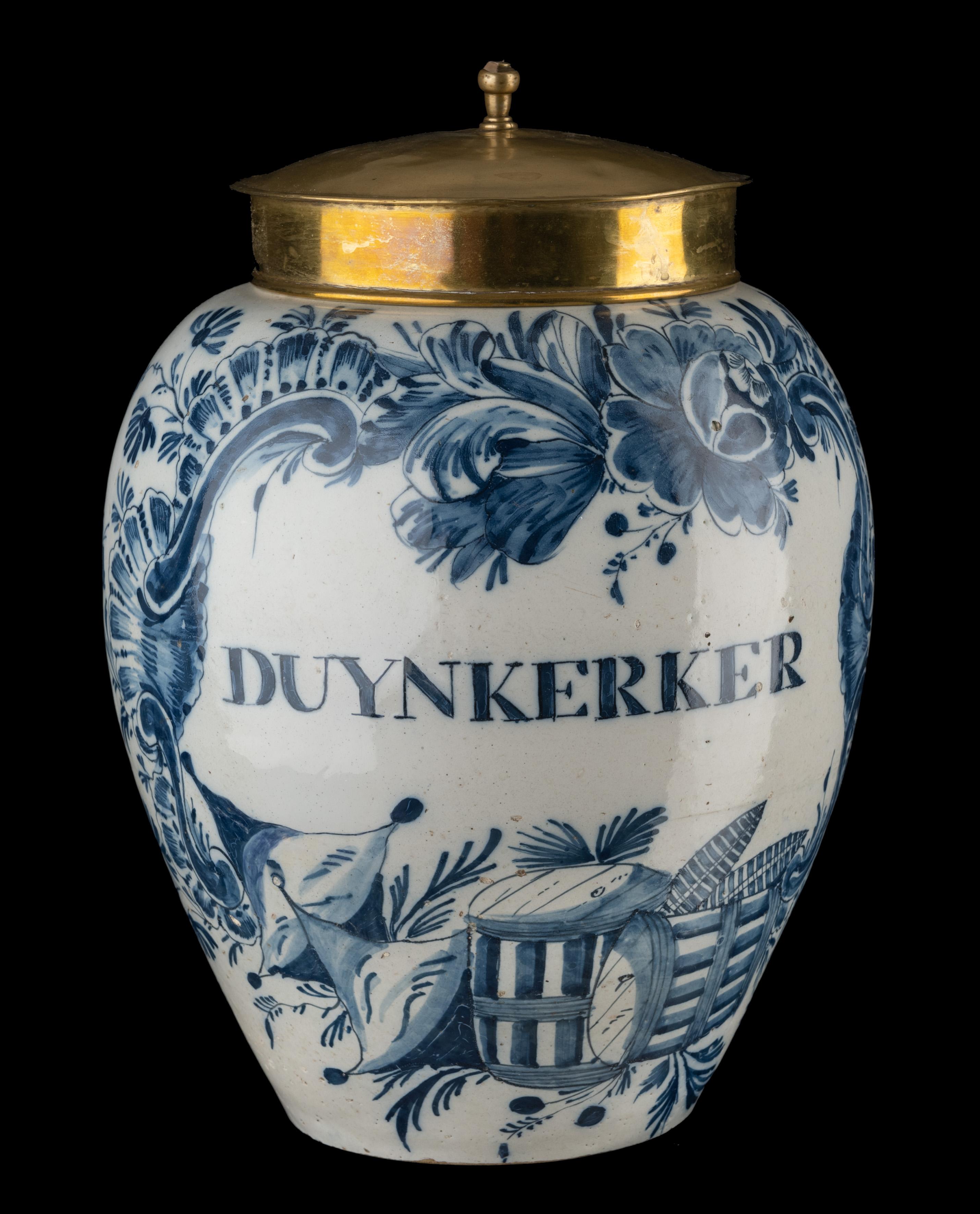 Blue and white DUYNKERKER tobacco jar
Delft, 1760-1780

The ovoid tobacco jar with copper lid has a groove on the shoulder at the top and a protruding rim. The jar is painted in blue with a cartouche containing the inscription DUYNKERKER. The